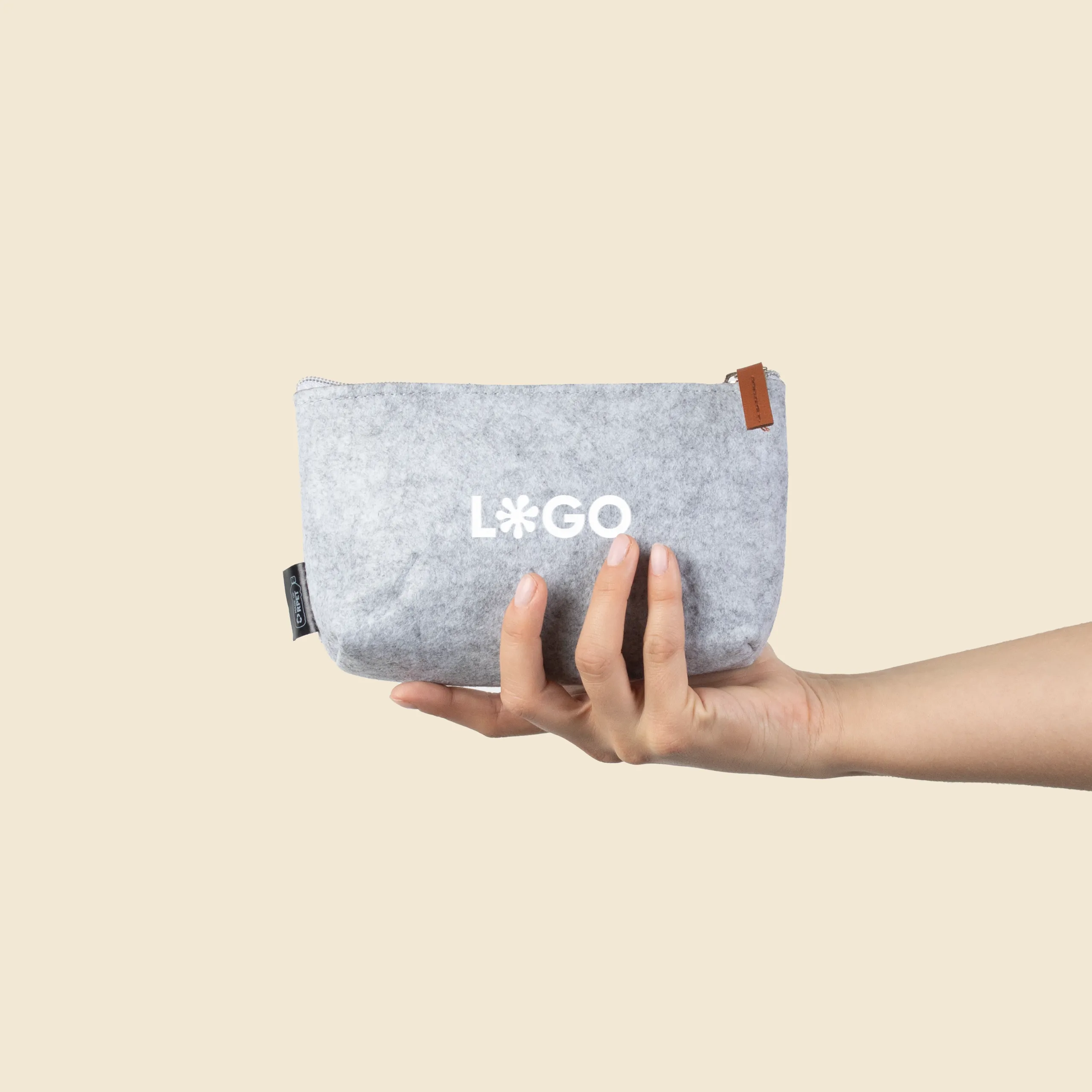 Trousse de voyage personnalisée en feutre ARLO Mano sujetando un neceser de viaje personalizado de color gris con la palabra logo en blanco