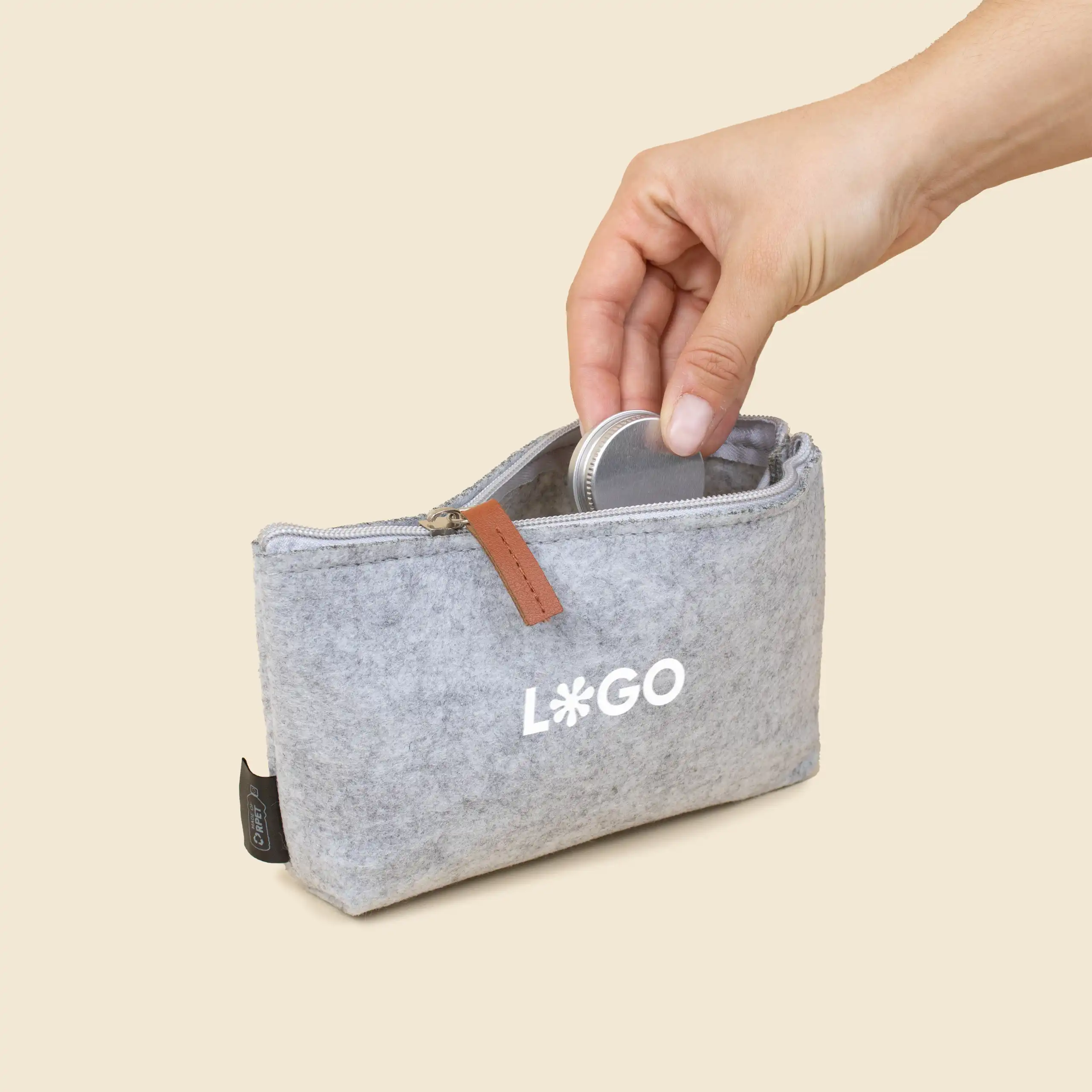 Neceser de viaje personalizado ARLO Mano metiendo un bálsamo labial dentro de un neceser de viaje de color gris personalizado con la palabra logo en blanco