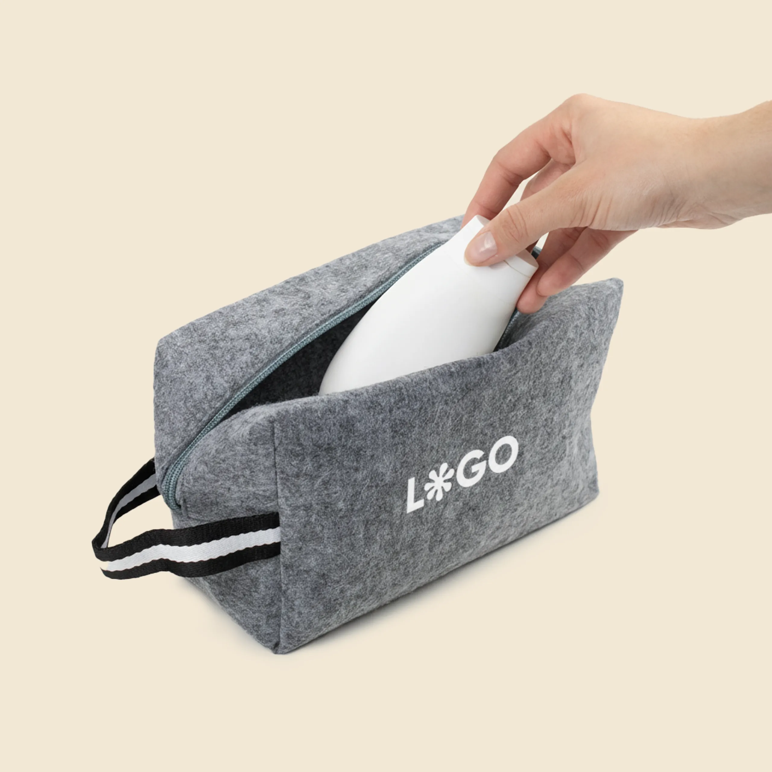 Mano metiendo un bote blanco en un neceser de fieltro con asa personalizado con la palabra 'logo' en blanco