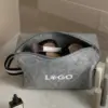Neceser de fieltro con asa personalizado con la palabra 'logo' en blanco en un baño con productos de cosmética en su interior
