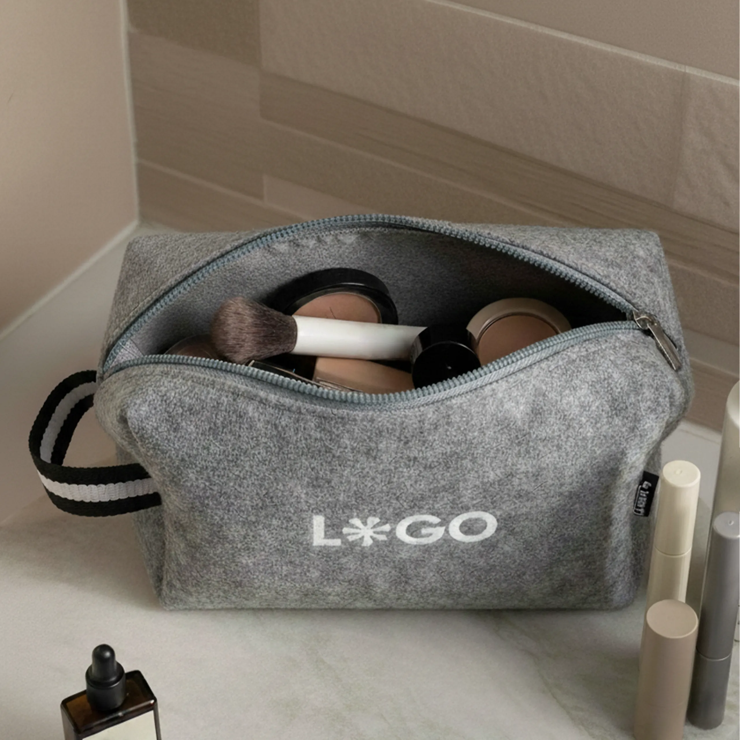 Neceser de fieltro con asa personalizado con la palabra 'logo' en blanco en un baño con productos de cosmética en su interior