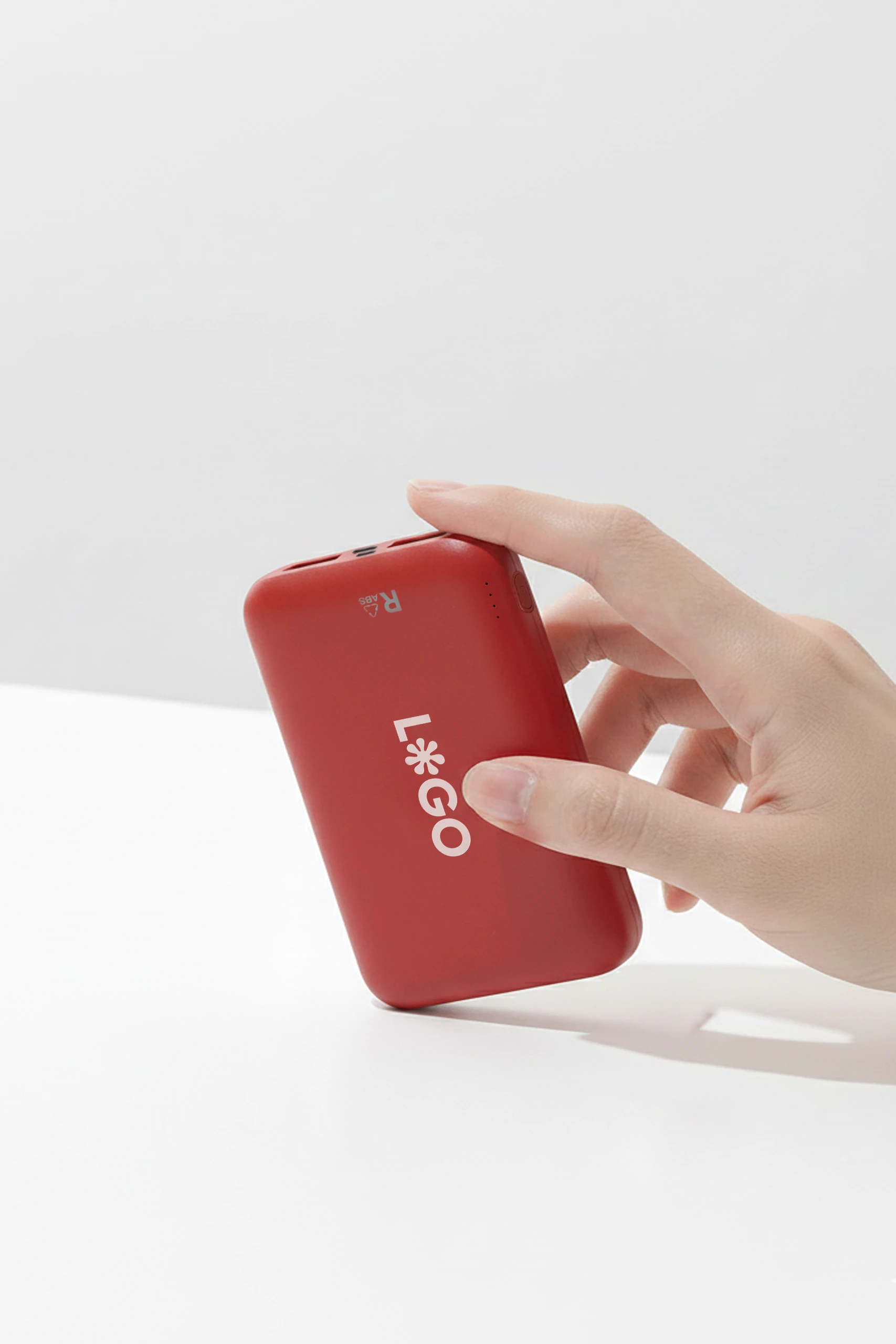 Mano mostrando una batería externa de color rojo personalizada con la palabra "LOGO" en blanco