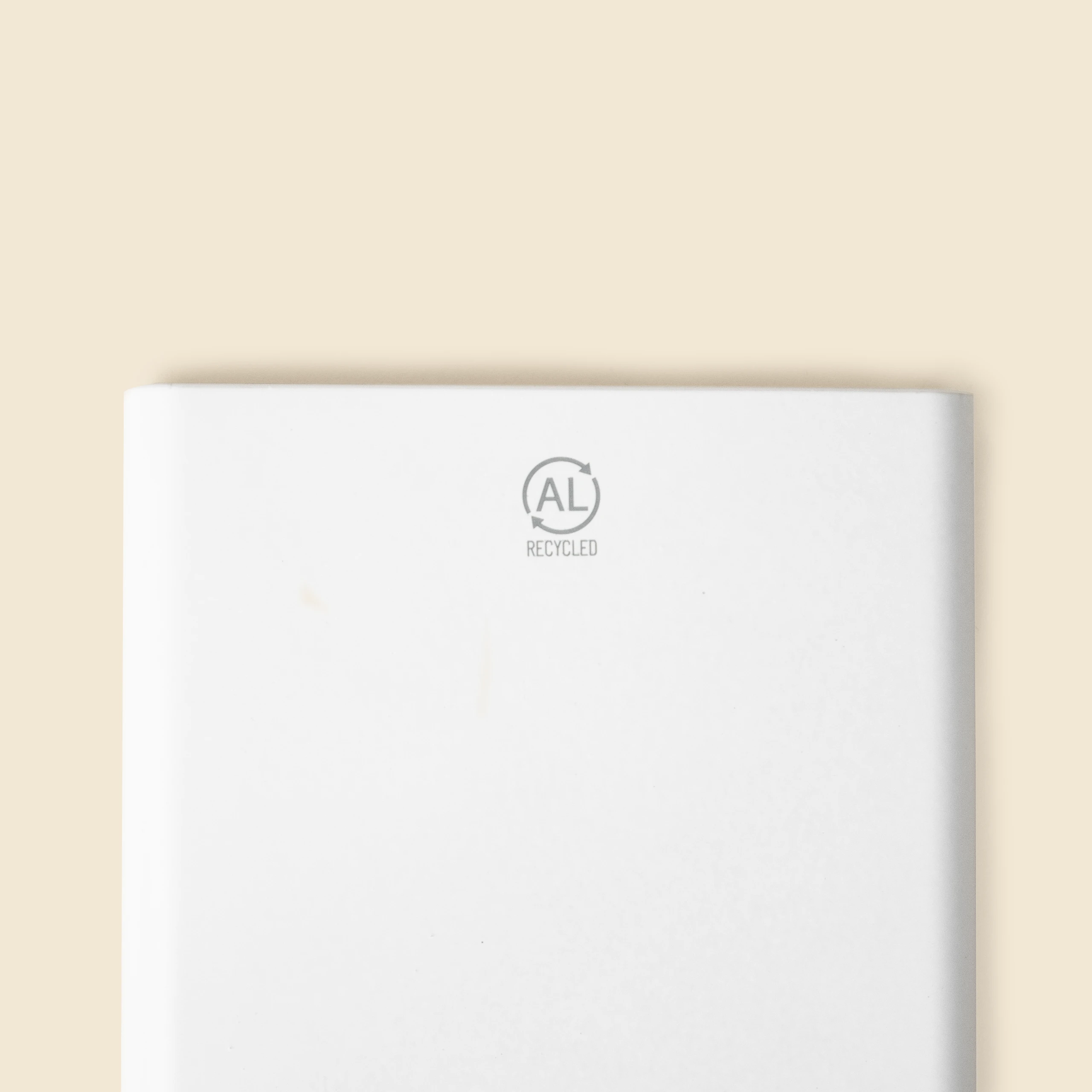 Detalle de distintivo impreso "AL recycled" en una batería portátil de color blanco