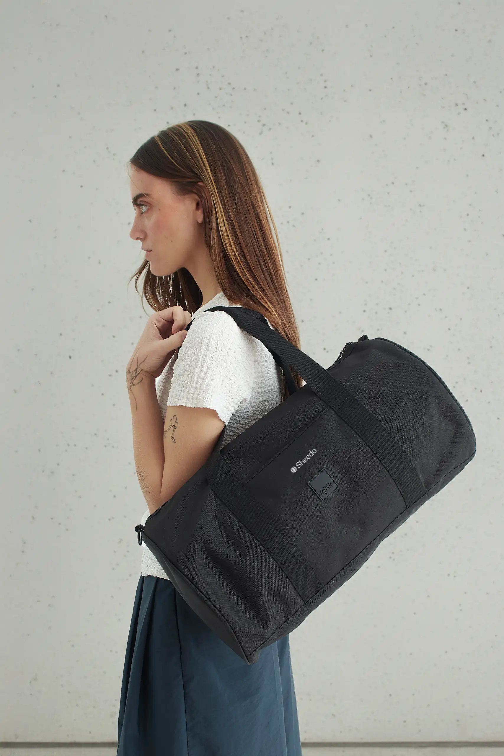 Chica llevando una bolsa de viaje negra de la marca Lefrik personalizada con el logotipo de "Sheedo"