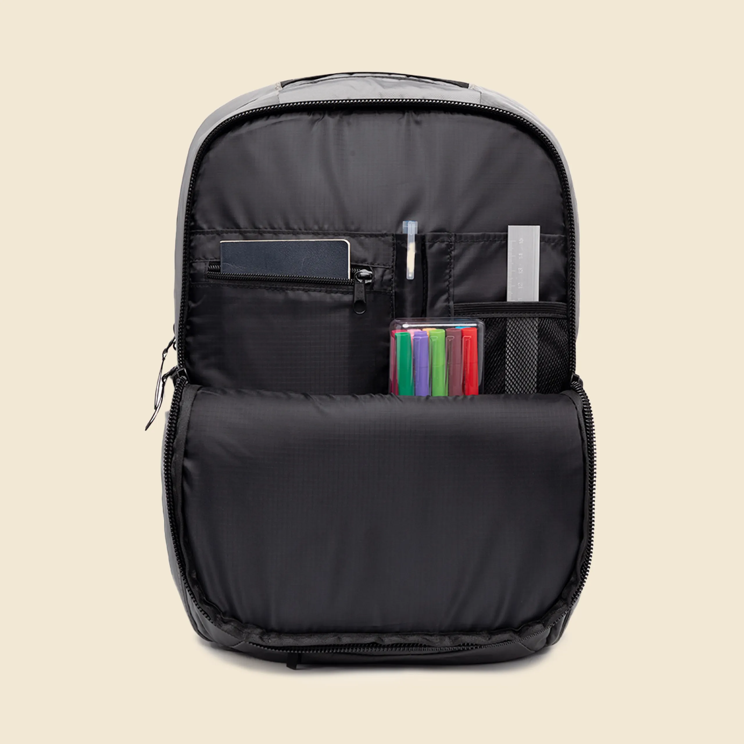 Mochila gris de la marca Lefrik abierta con rotuladores, una regla y un bloc de notas en su interior