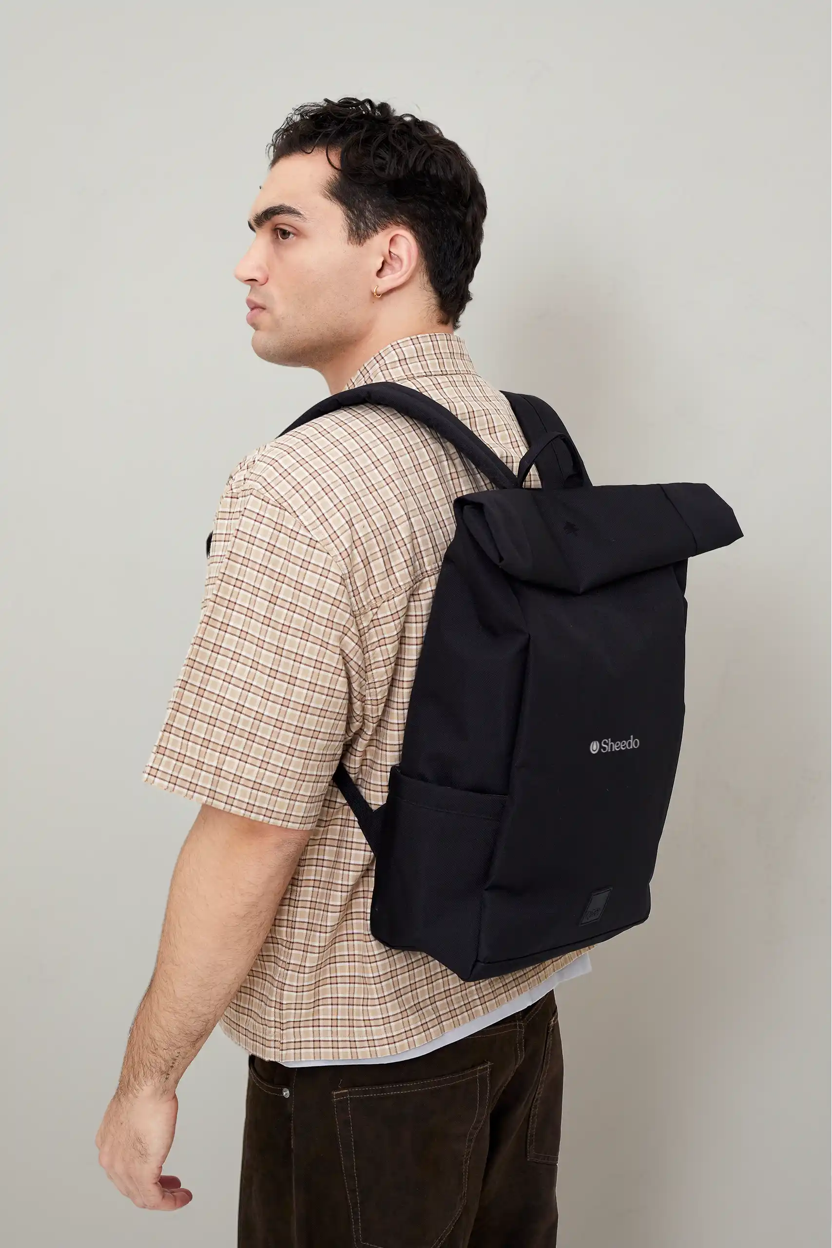 Chico llevando en la espalda una mochila roll-top negra de la marca Lefrik personalizada con el logo de Sheedo en blanco