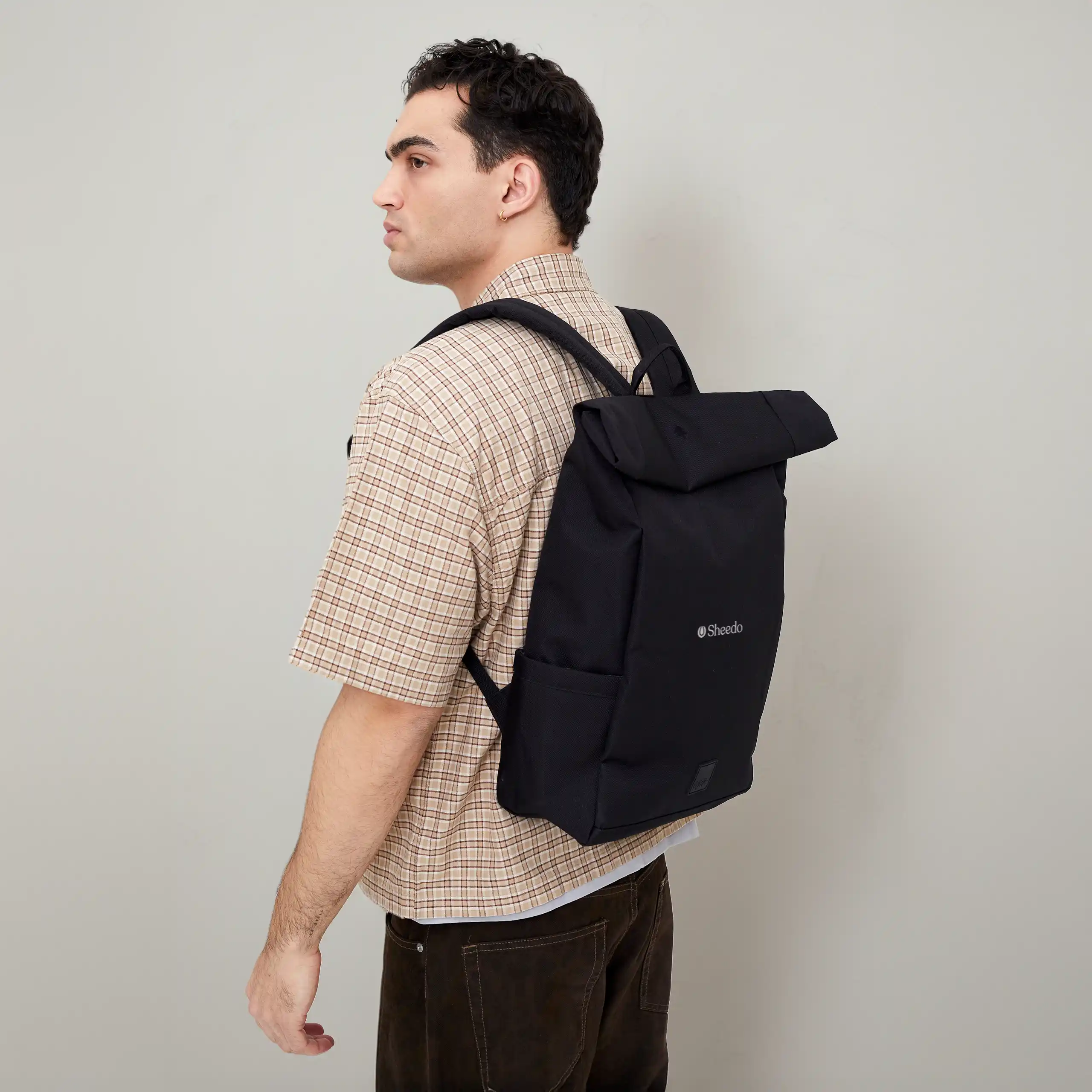 Mochila personalizada LEFRIK ROLL Chico llevando en la espalda una mochila roll-top negra de la marca Lefrik personalizada con el logo de Sheedo en blanco