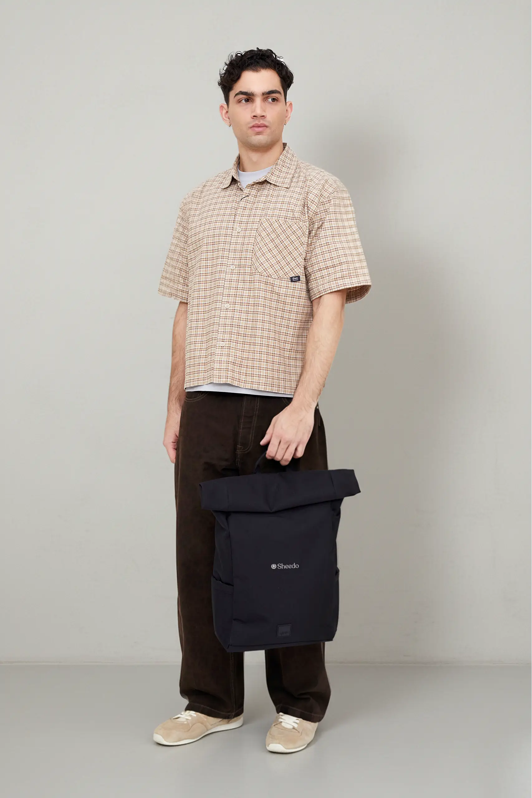 Chico llevando en la mano una mochila roll-top negra de la marca Lefrik personalizada con el logo de Sheedo en blanco