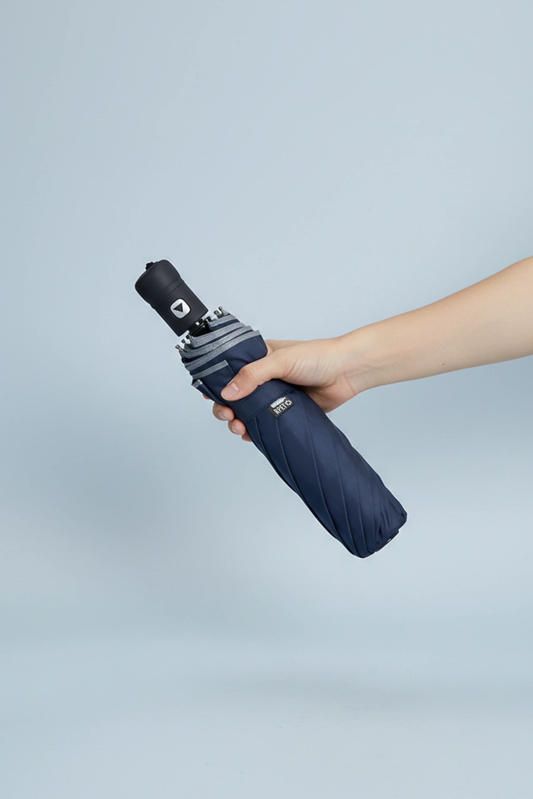 Paraguas azul oscuro con logo y sujeto por una mano. Con apertura automática y plegable.