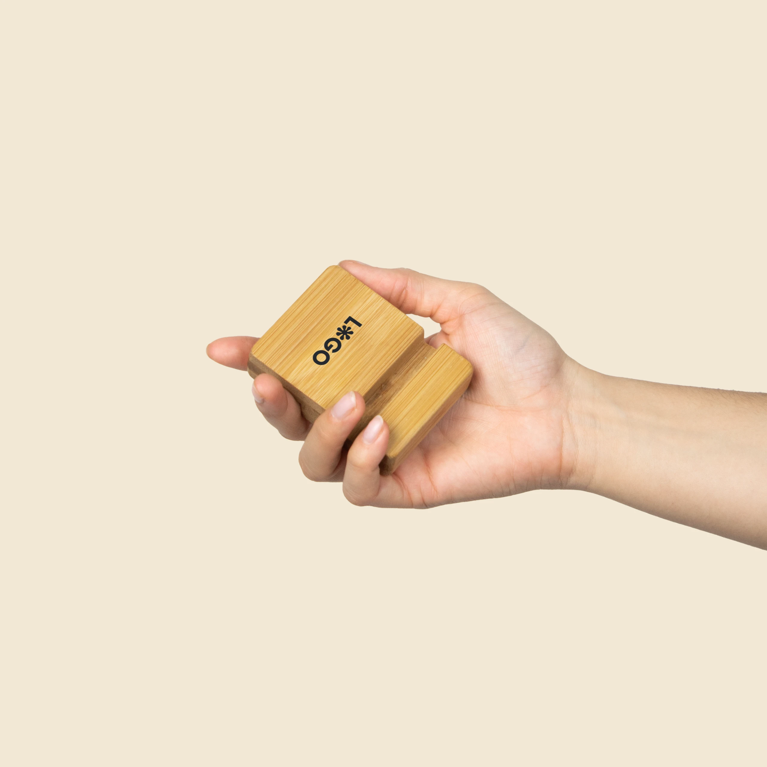 Mano sujetando un soporte para móvil de bambú personalizado con la palabra "LOGO" impresa en negro