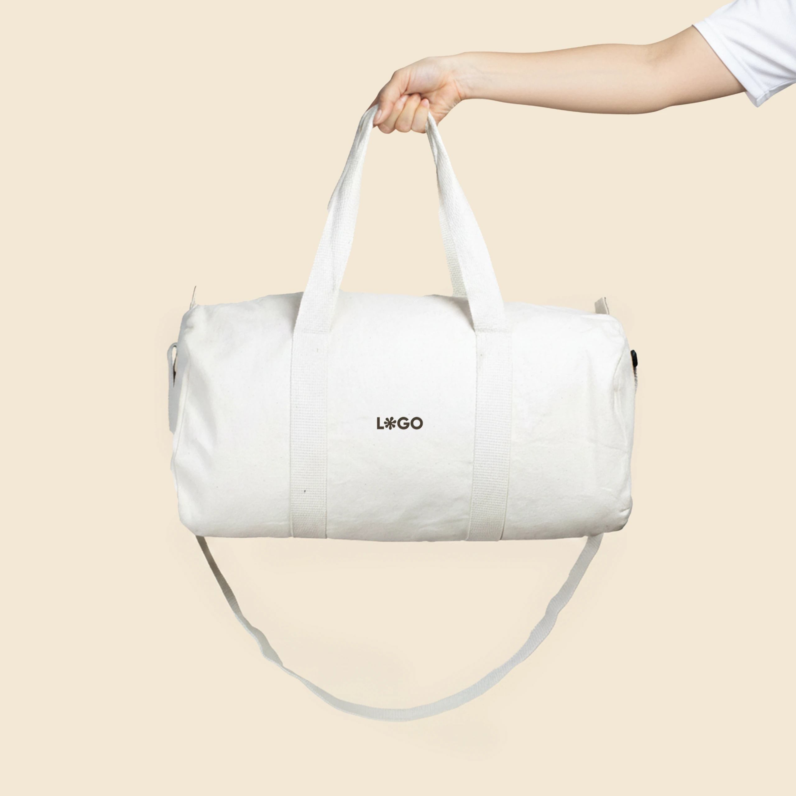 Bolsa de gimnasio personalizada sujeta por un brazo con camiseta blanca de algodón. De algodón reciclado y color beige. Con personalización a todo color marrón.