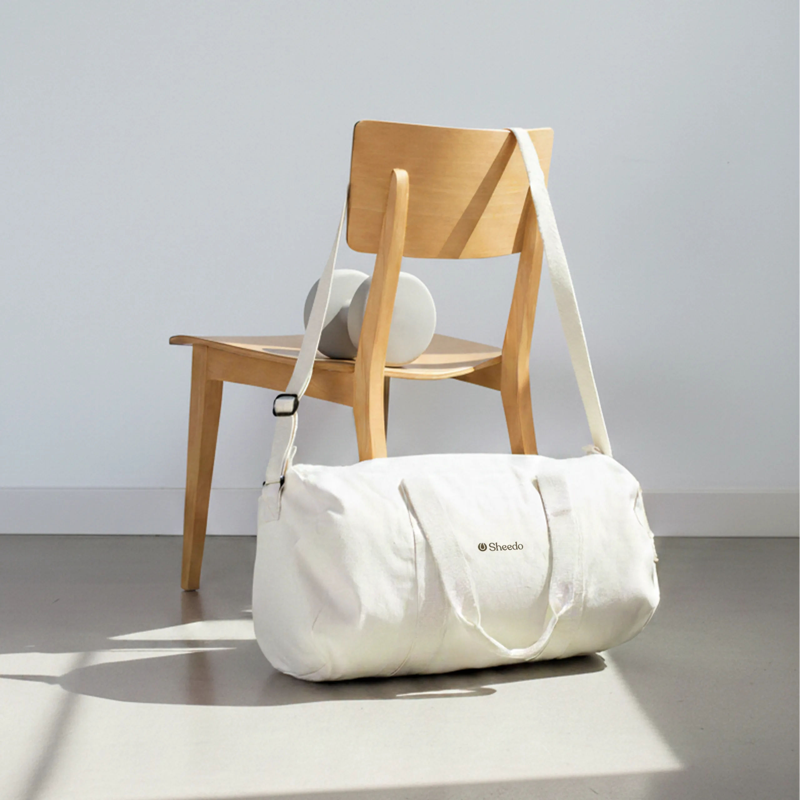 Bolsa de gimnasio personalizada. De algodón reciclado y color beige. Con personalización a todo color marrón. Sujeta por una silla de madera en un espacio deportivo.