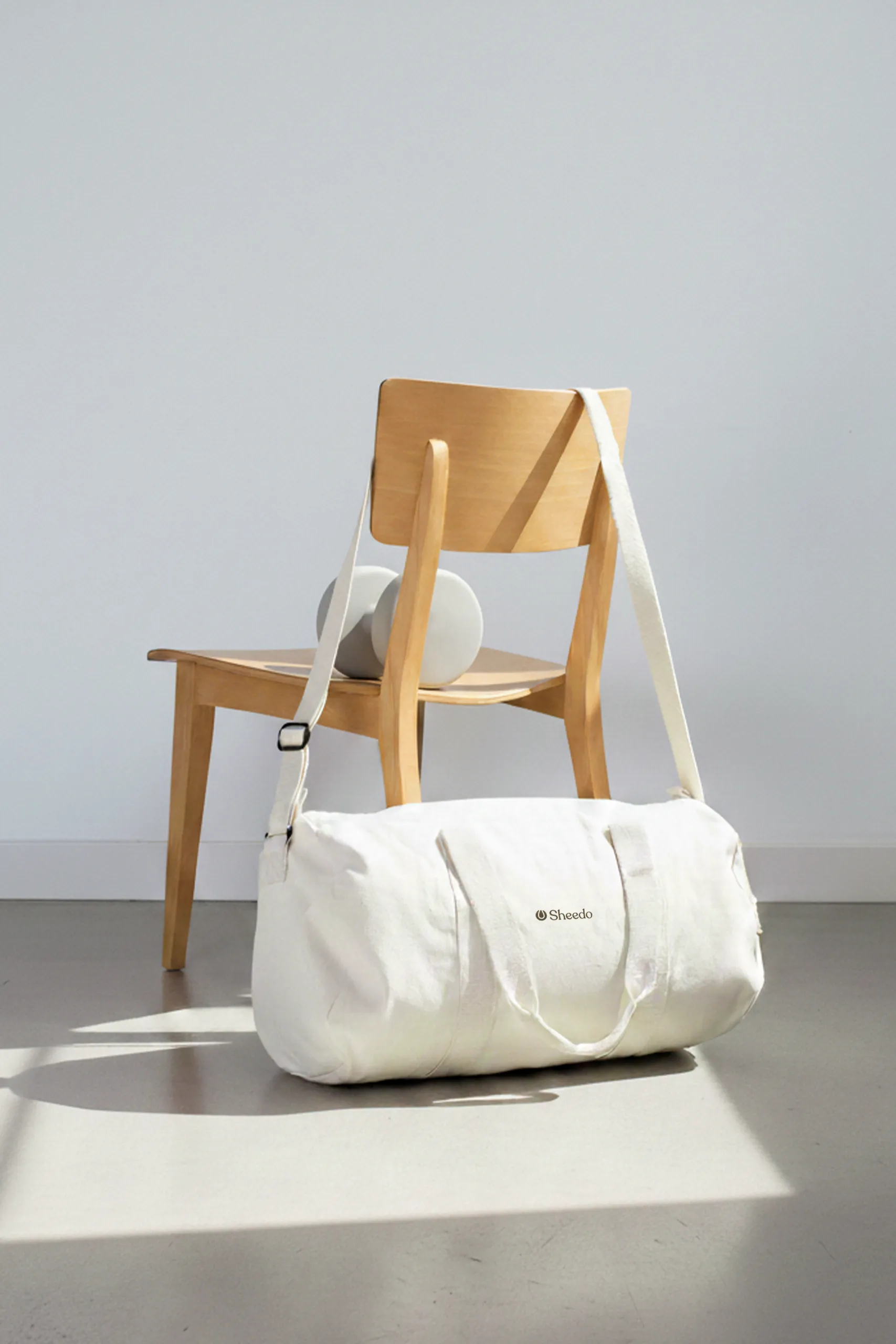 Bolsa de gimnasio personalizada. De algodón reciclado y color beige. Con personalización a todo color marrón. Sujeta por una silla de madera en un espacio deportivo.