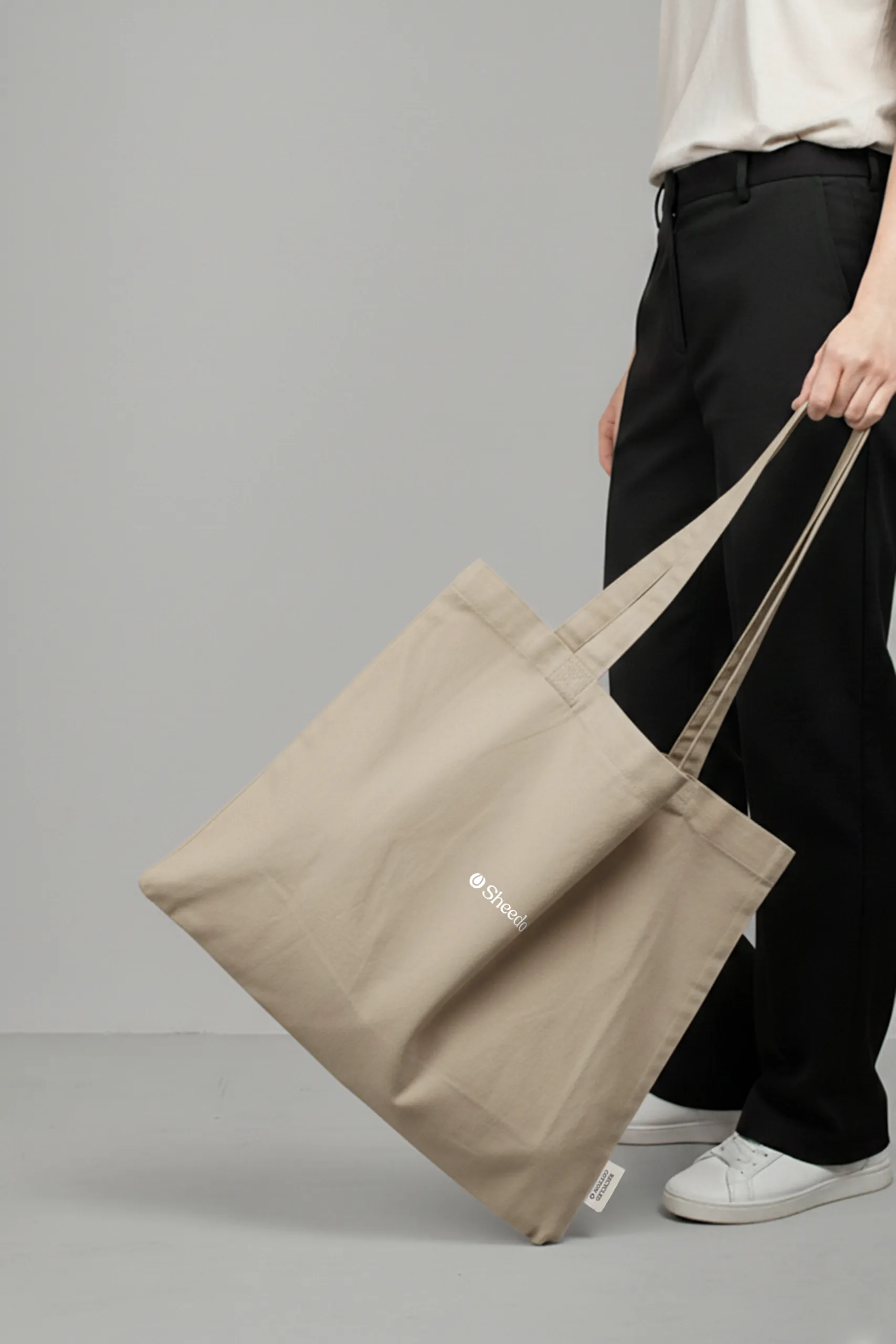 Bolsa tote personalizada. Fabricada en algodón reciclado. De color beige y personalización a todo color. Con una persona sujetándola.