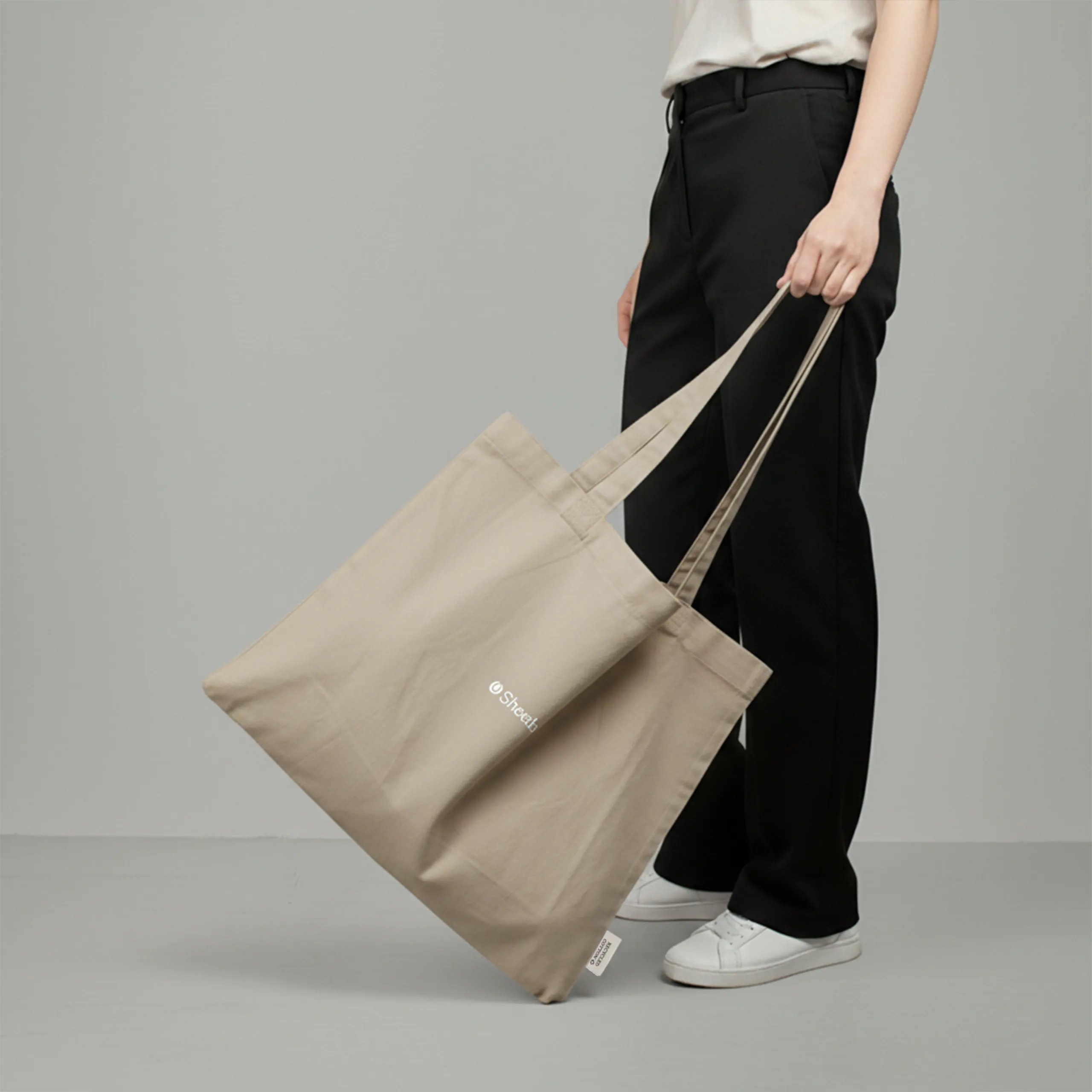 Bolsa tote personalizada. Fabricada en algodón reciclado. De color beige y personalización a todo color. Con una persona sujetándola.