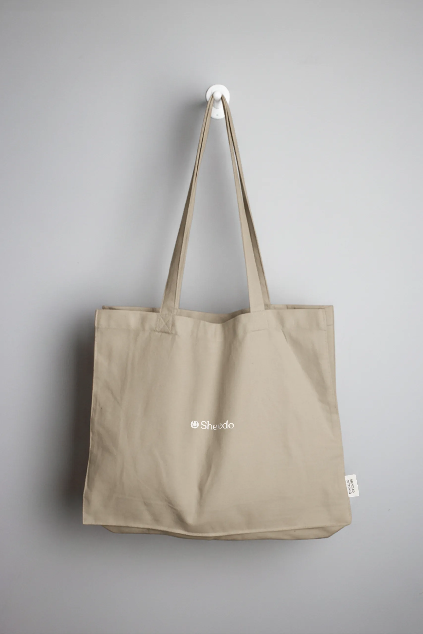 Bolsa tote personalizada colgada. Fabricada en algodón reciclado. De color beige y personalización a todo color.