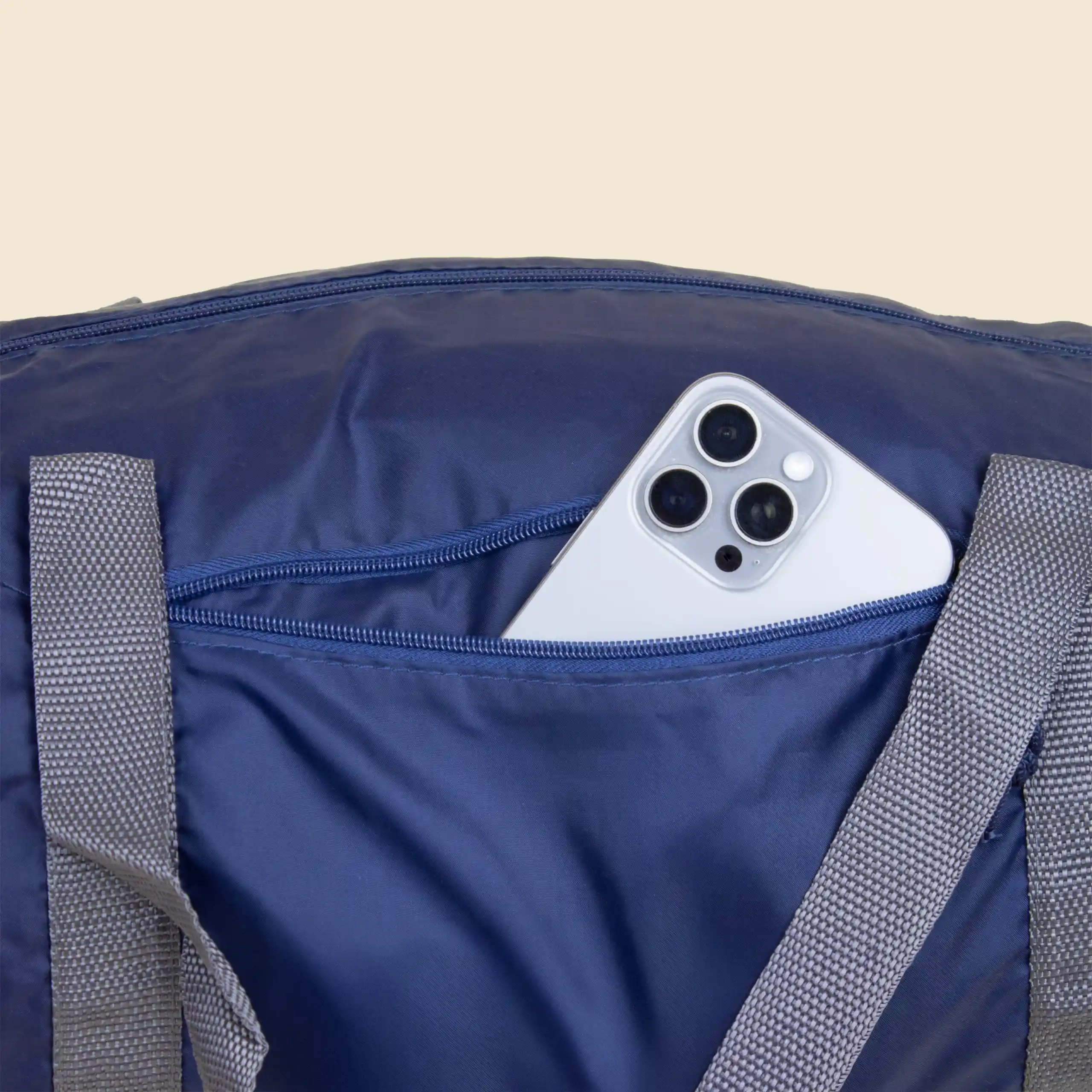 Bolsillo exterior de cremallera de la mochila de deporte personalizada con un iphone dentro. De color azul marino con asas grises y diseño en blanco. Elaborado a partir de plástico reciclado (RPET).