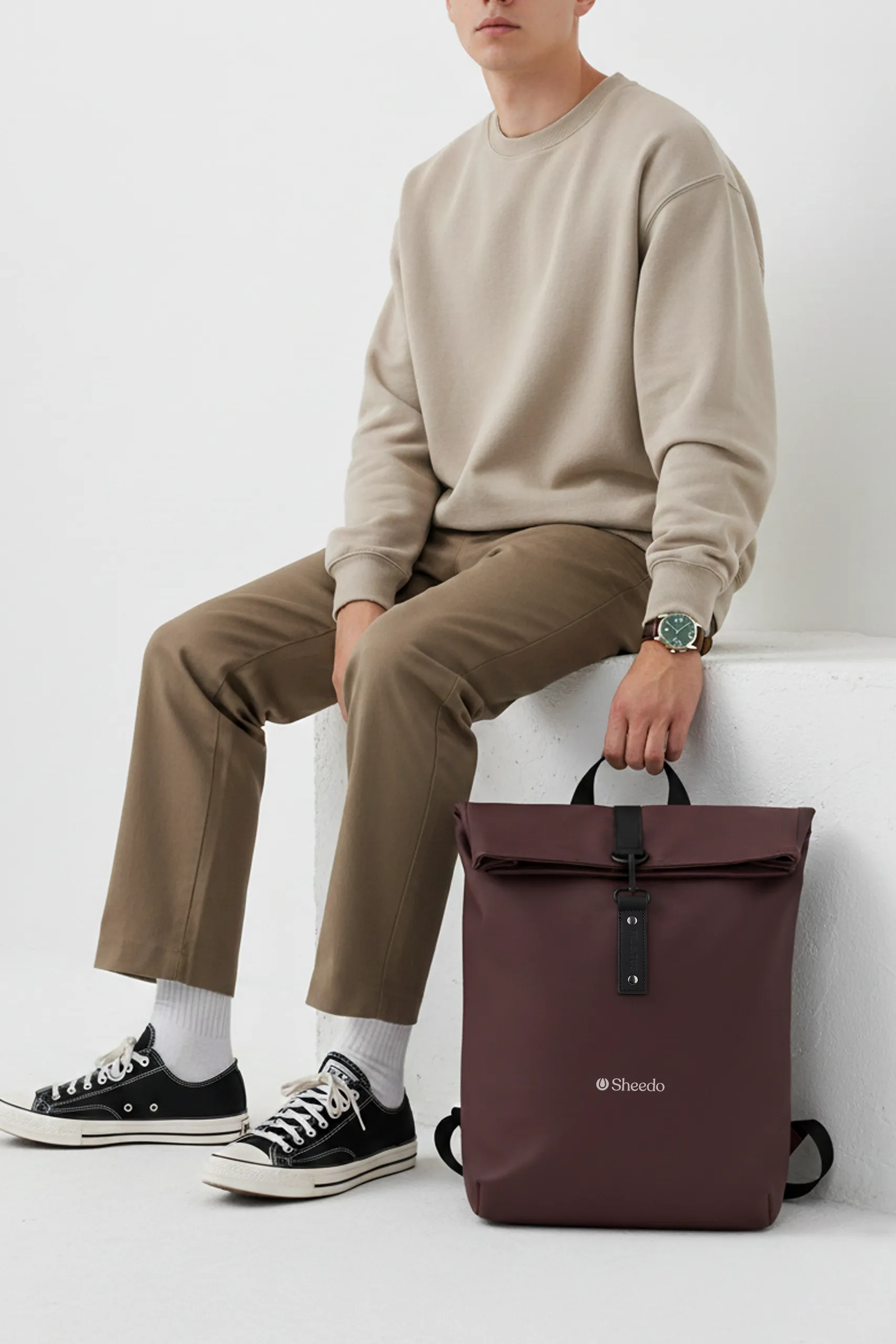 Mochila enrollable de la marca Pilatus , de color bourdeos y con personalización a 1 tinta. Sujeta por un chico en una sala blanca.