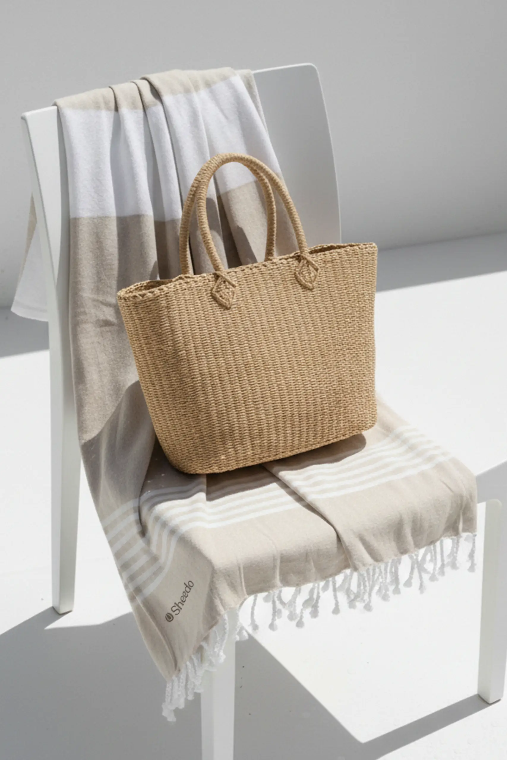 Pareo personalizado, 100% algodón , a rayas de color beige y flecos. Colgado en una silla al sol y con una cesta de mimbre.