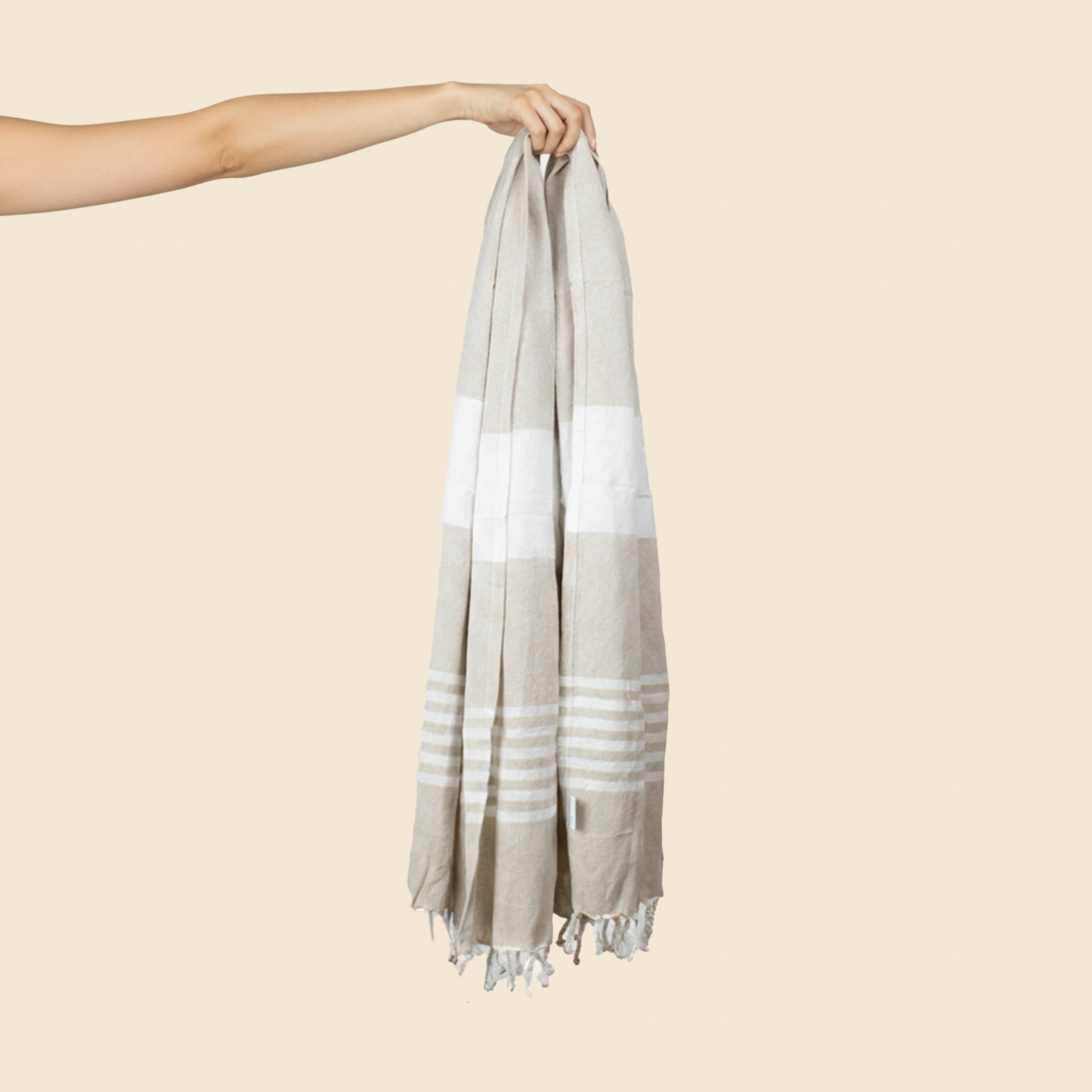 Pareo personalizado, 100% algodón , a rayas de color beige y flecos. Sujeto por una mano.