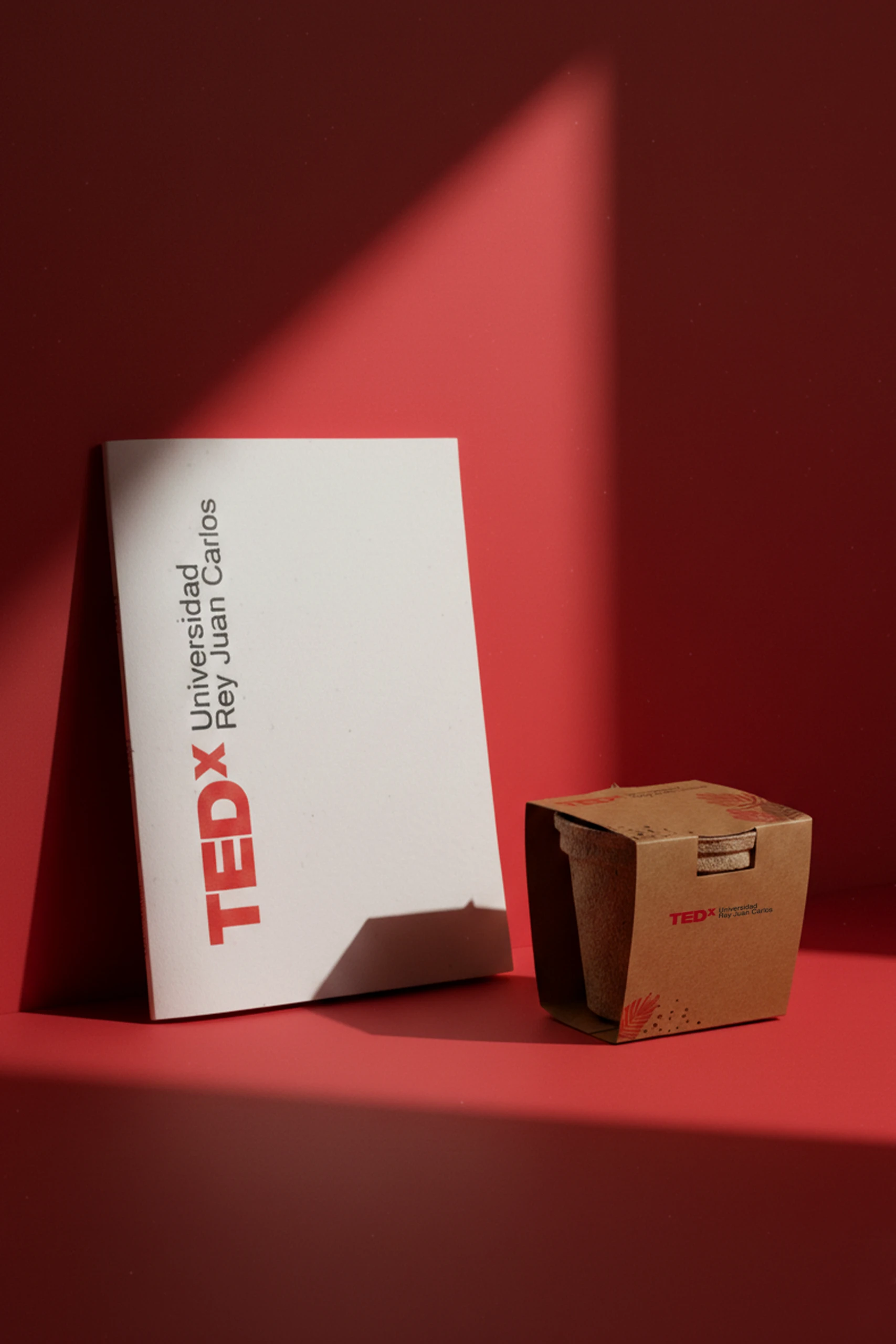Cuaderno plantable blanco y kit plantable personalizados con el logo de la marca TEDx, sobre un fondo rojo