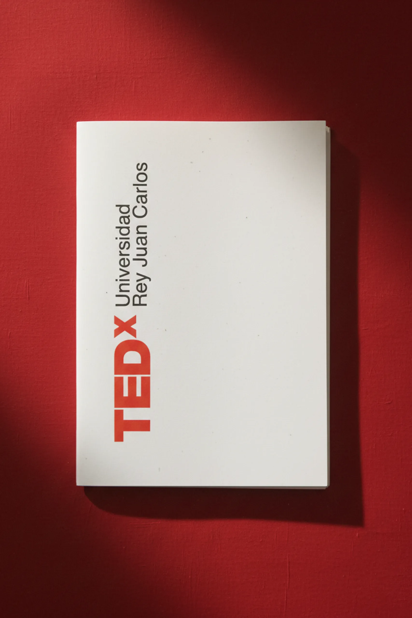 Cuaderno plantable blanco personalizado con el logo de la marca TEDx, sobre un fondo rojo