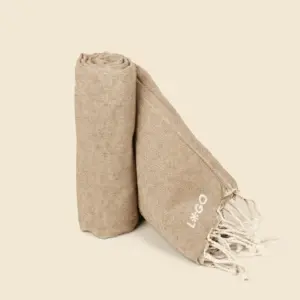 Toalla de playa personalizada con logo blanco. Fabricado de RPET. De color beige y con flecos.