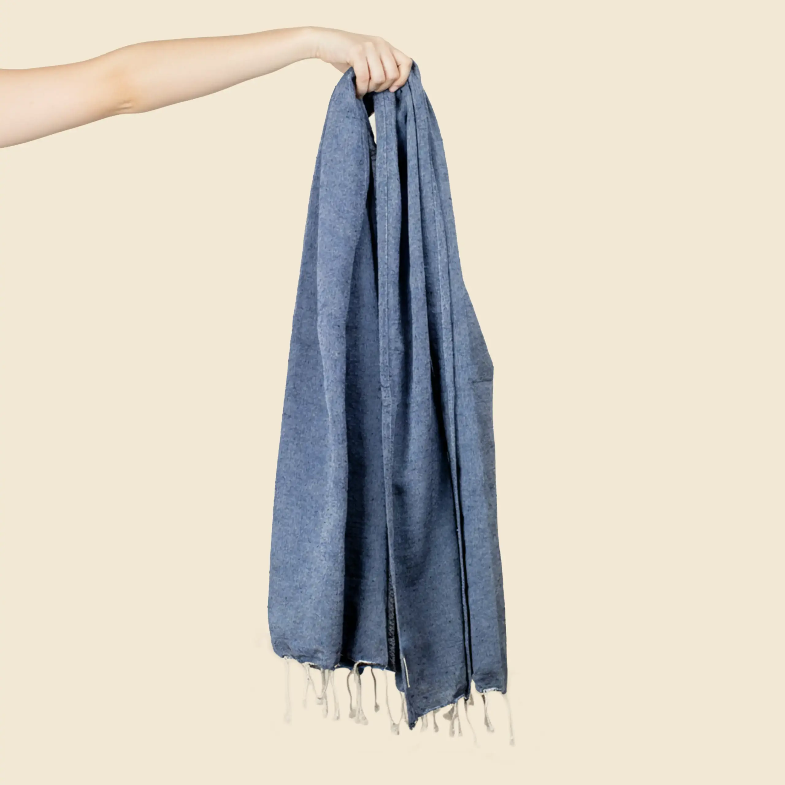 Toalla de playa personalizada_CAPRI Toalla de playa personalizada con logo blanco. Fabricado de RPET. De color azul y con flecos. Sujeta por una mano.