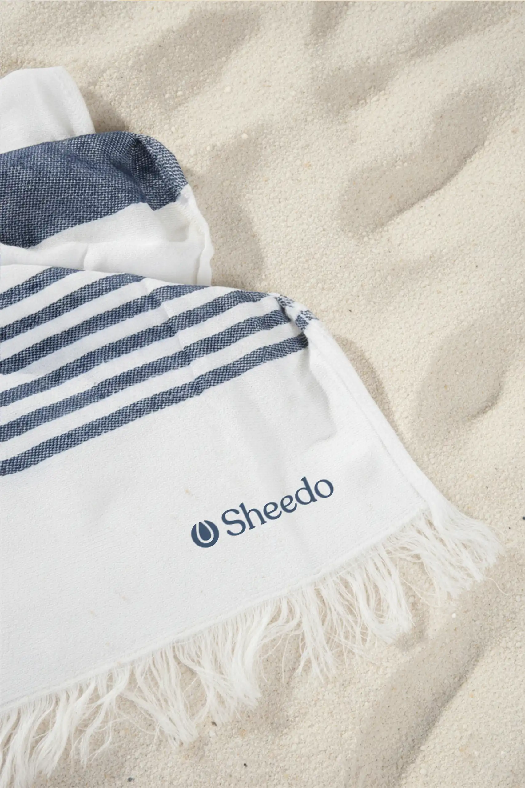 Toalla pareo personalizado. Con flecos y de color azul y blanco a rayas. Extendido en la playa.