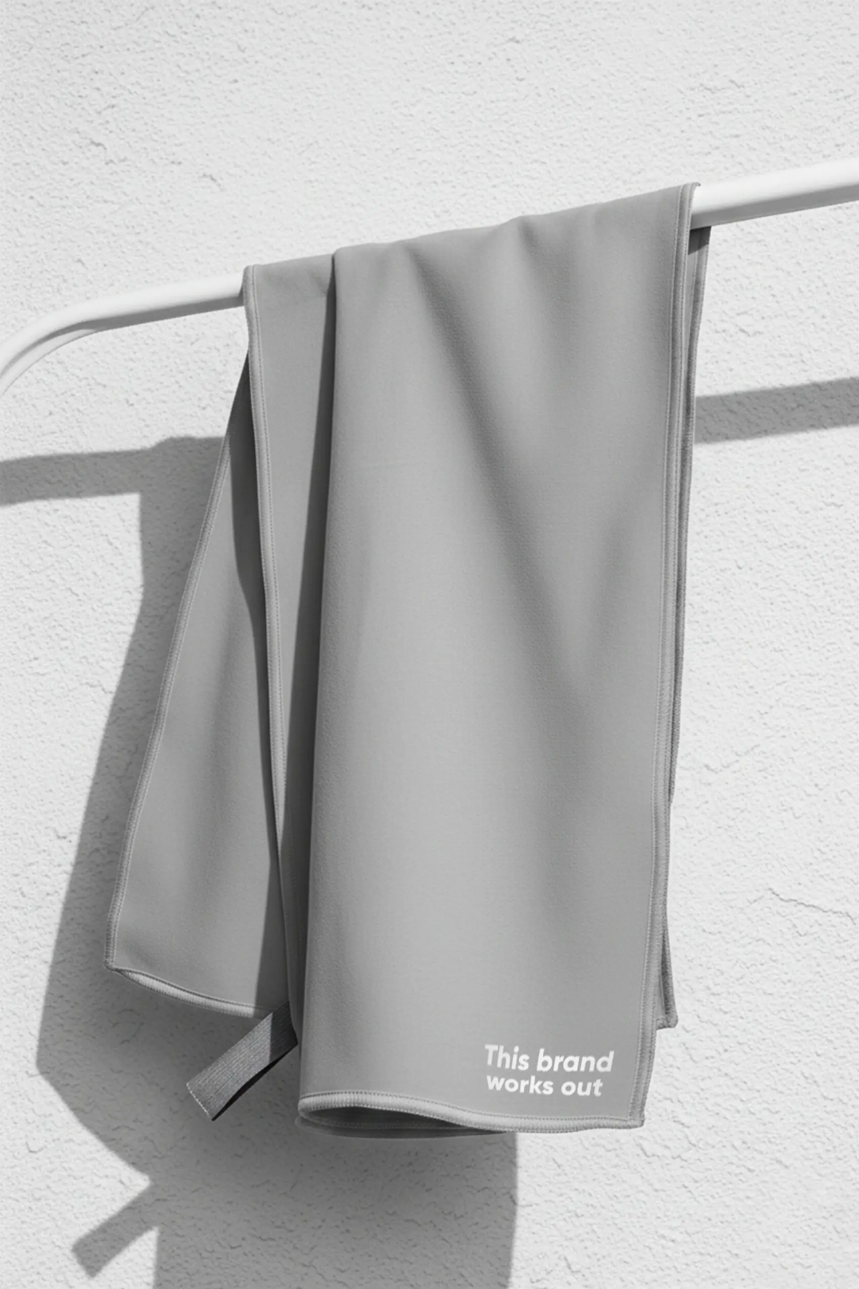 Toalla pequeña gris personalizada con un texto en blanco y colgada de una barra de metal blanca