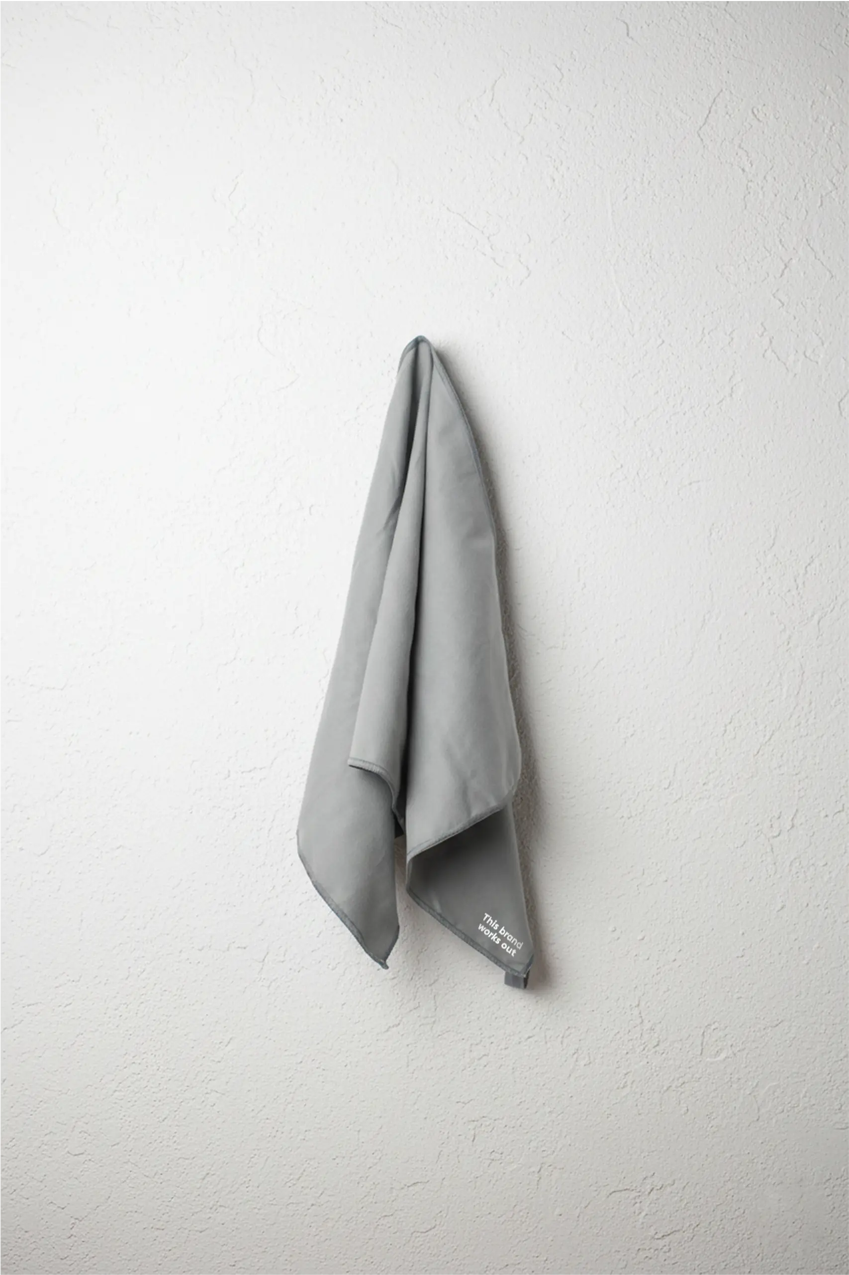 Toalla pequeña gris personalizada con un texto en blanco y colgada de una pared blanca