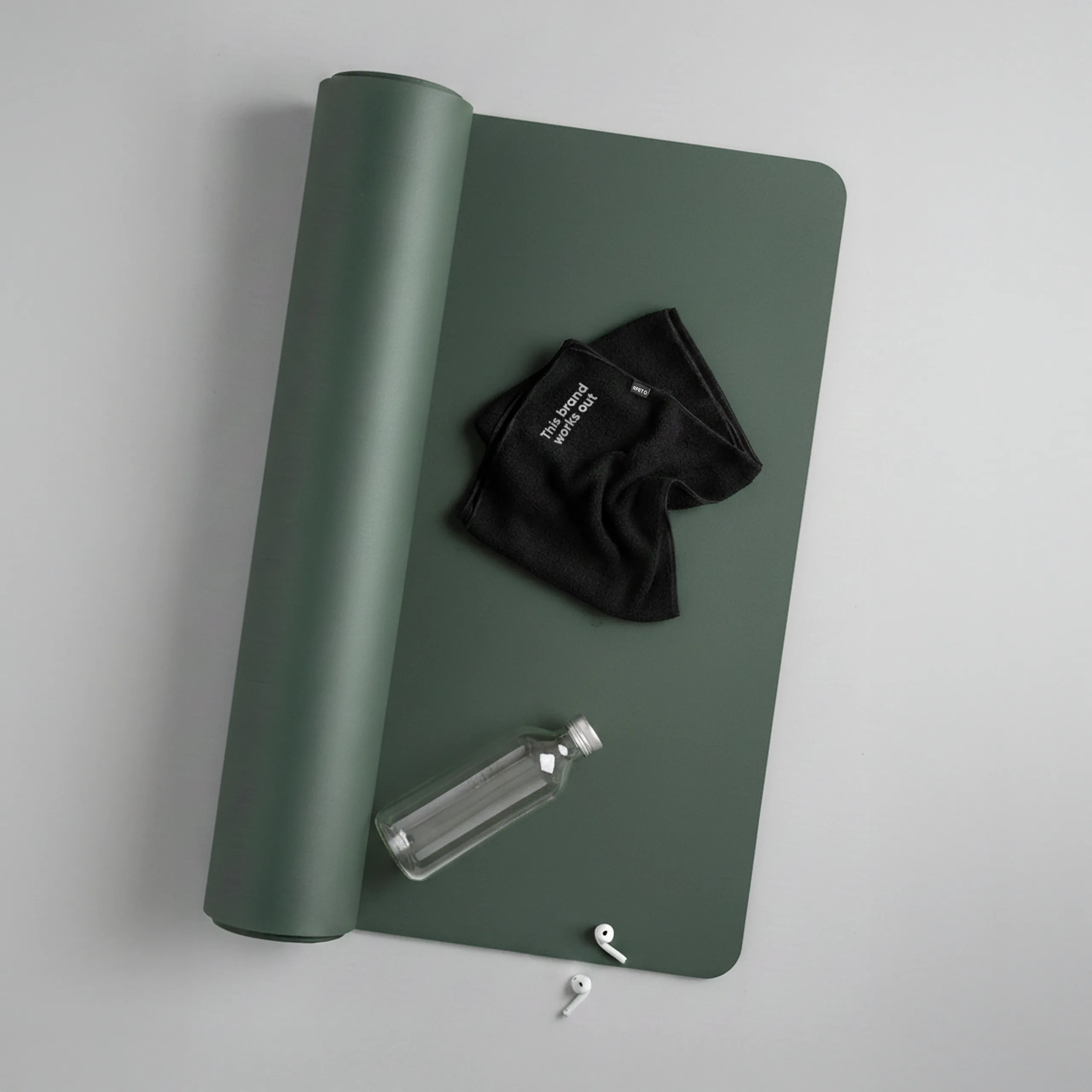 Toalla personalizada de gimnasio, de color negro y de material rpet. Con bordado en esquina de frase. Con esterilla de yoga , botella de cristal y auriculares.