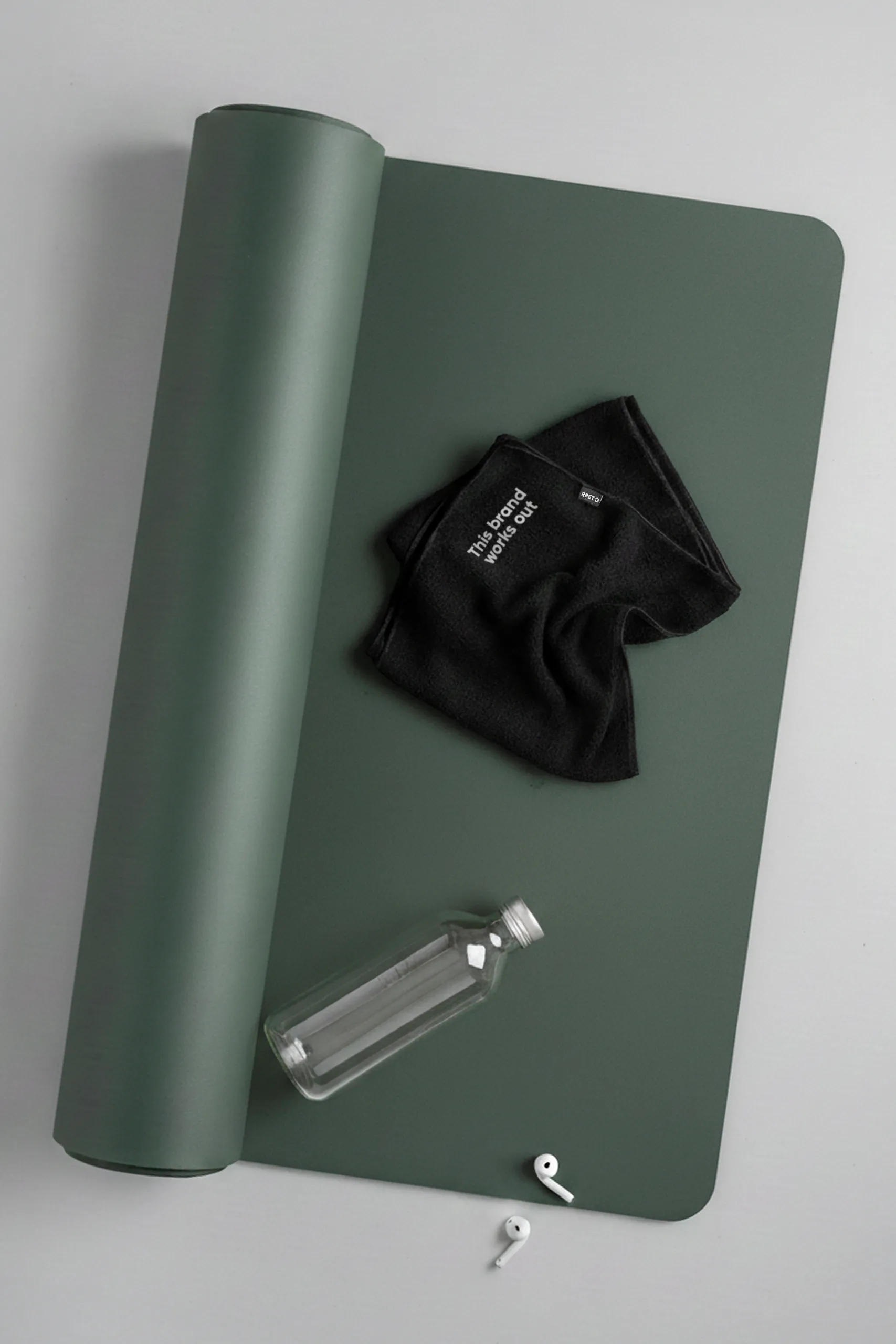 Toalla personalizada de gimnasio, de color negro y de material rpet. Con bordado en esquina de frase. Con esterilla de yoga , botella de cristal y auriculares.