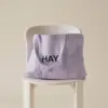 Bolsa de diseño de la marca HAY con impresión a todo color y a una tinta. De color lila. Apoyada en una silla blanca.