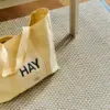 Bolsa de diseño de la marca HAY con impresión a todo color y a una tinta. De color amarilla. Apoyada en el suelo.