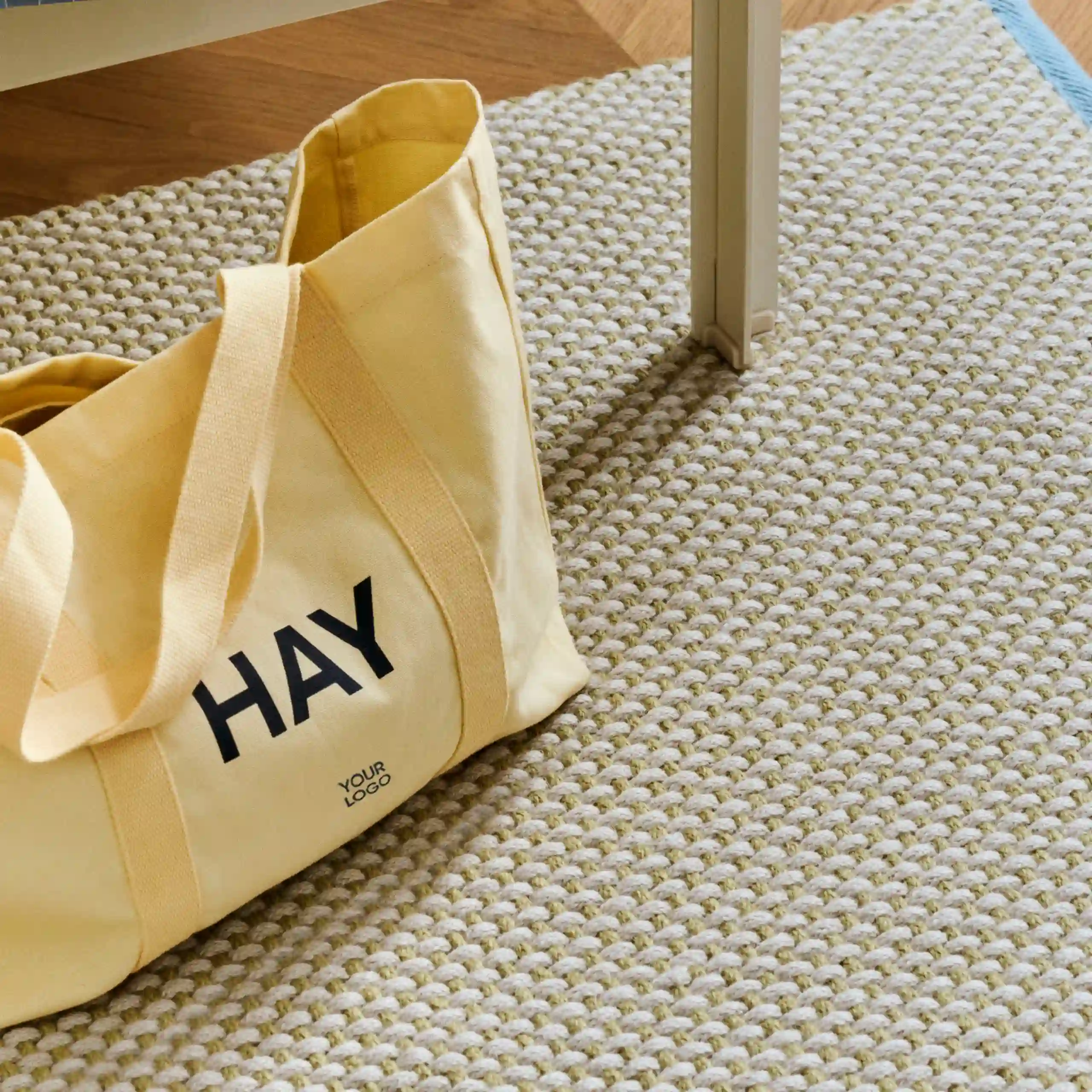 Bolsa de diseño de la marca HAY con impresión a todo color y a una tinta. De color amarilla. Apoyada en el suelo.