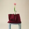 Bolsa de diseño de la marca HAY con impresión a todo color y a una tinta. De color rojo. Apoyada en una silla azul y con una flor.