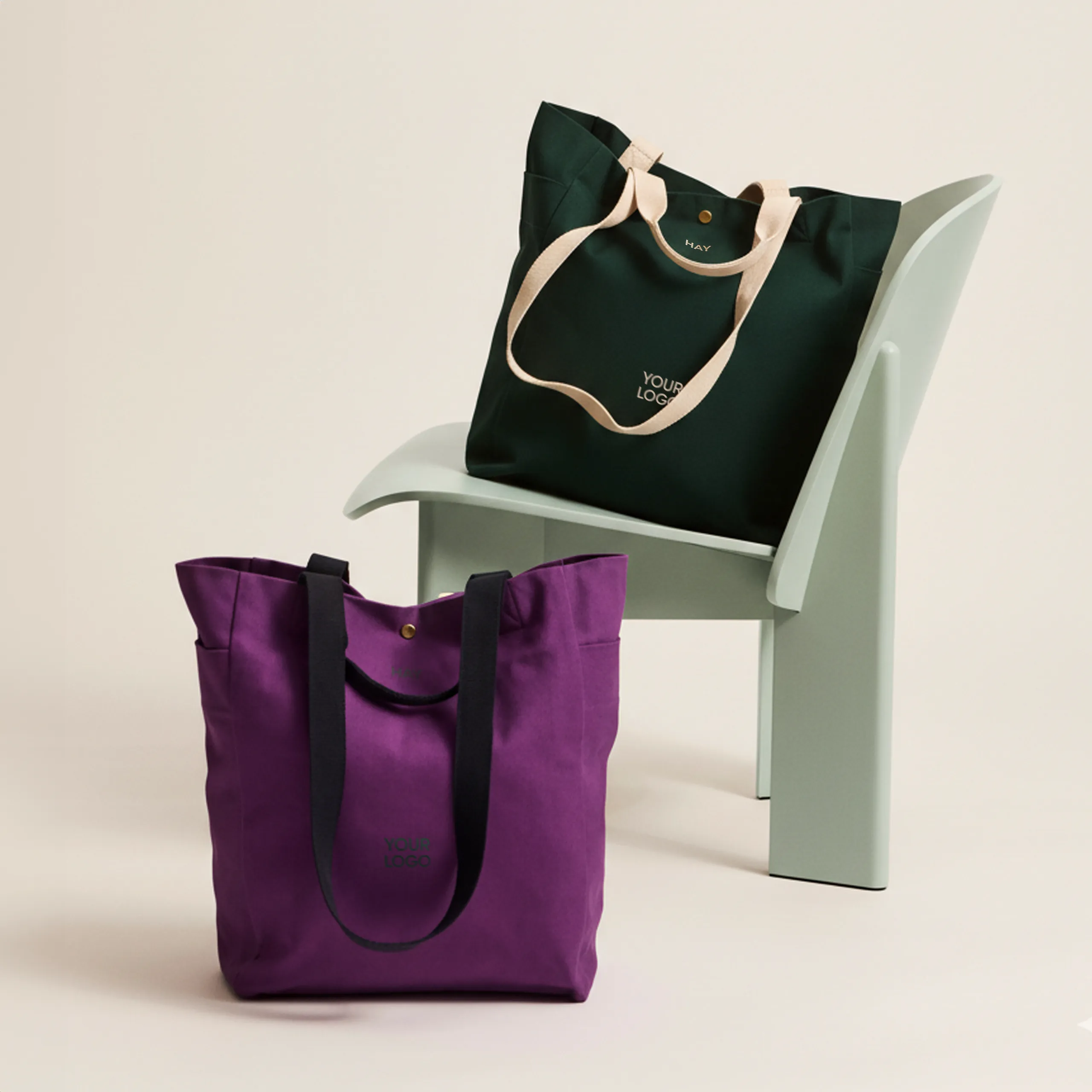 Bolsa tote de algodón orgánico de la marca HAY. Personalizable a todo color y a un color. Colocadas en una silla blanca.