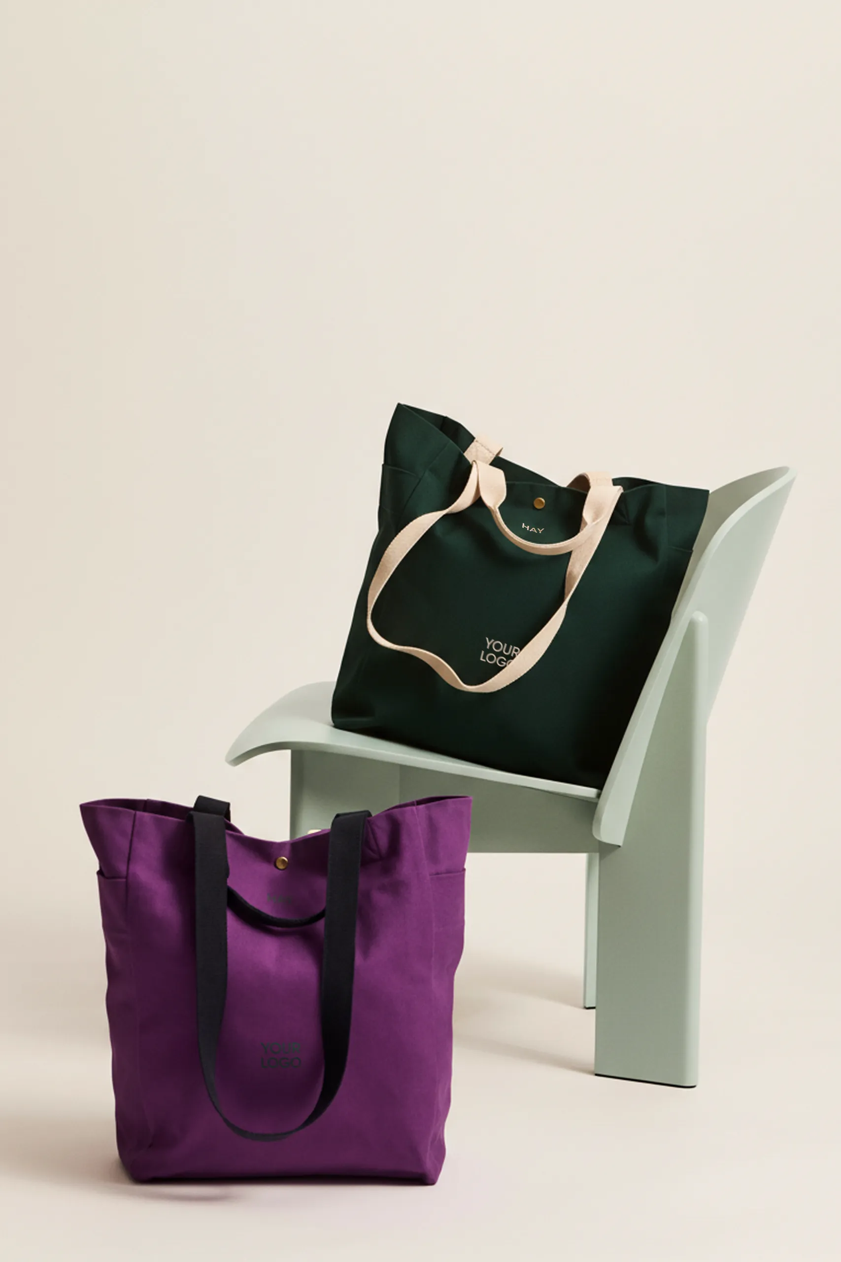 Bolsa tote de algodón orgánico de la marca HAY. Personalizable a todo color y a un color. Colocadas en una silla blanca.