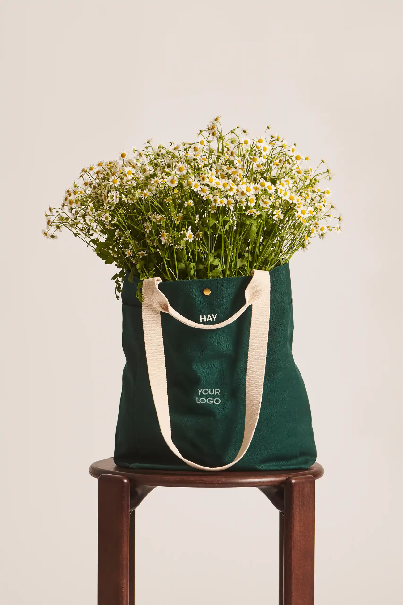 Bolsa tote de algodón orgánico de la marca HAY. Personalizable a todo color y a un color. De color verde y asas beige. Con un ramo de margaritas saliendo de la bolsa.