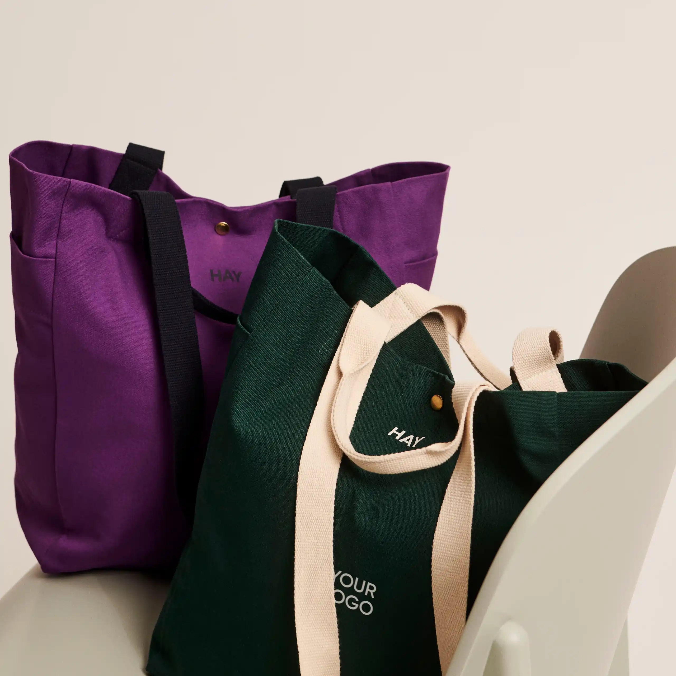 Bolsa tote de algodón orgánico de la marca HAY. Personalizable a todo color y a un color. Colocadas en una silla blanca.