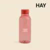 Botella minimalista de la marca HAY. De color rojo transparente. Diseñada por el reconocido Naoto Fukasawa . Fabricada en PET reciclado.
