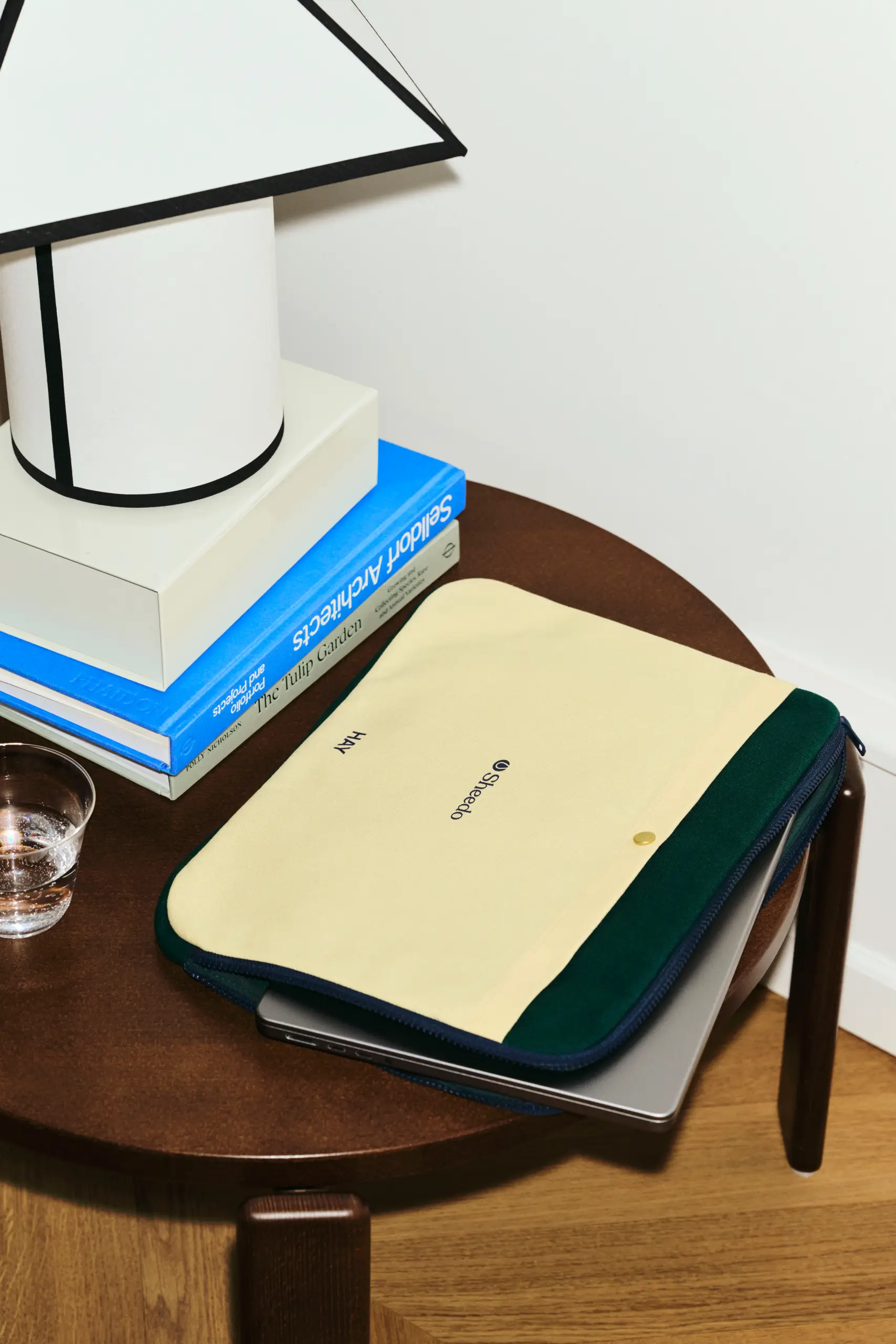 Funda de portátil de la marca HAY. Con botón dorado y cremallera. Combinado de colores amarillo y verde. En una mesa de madera.