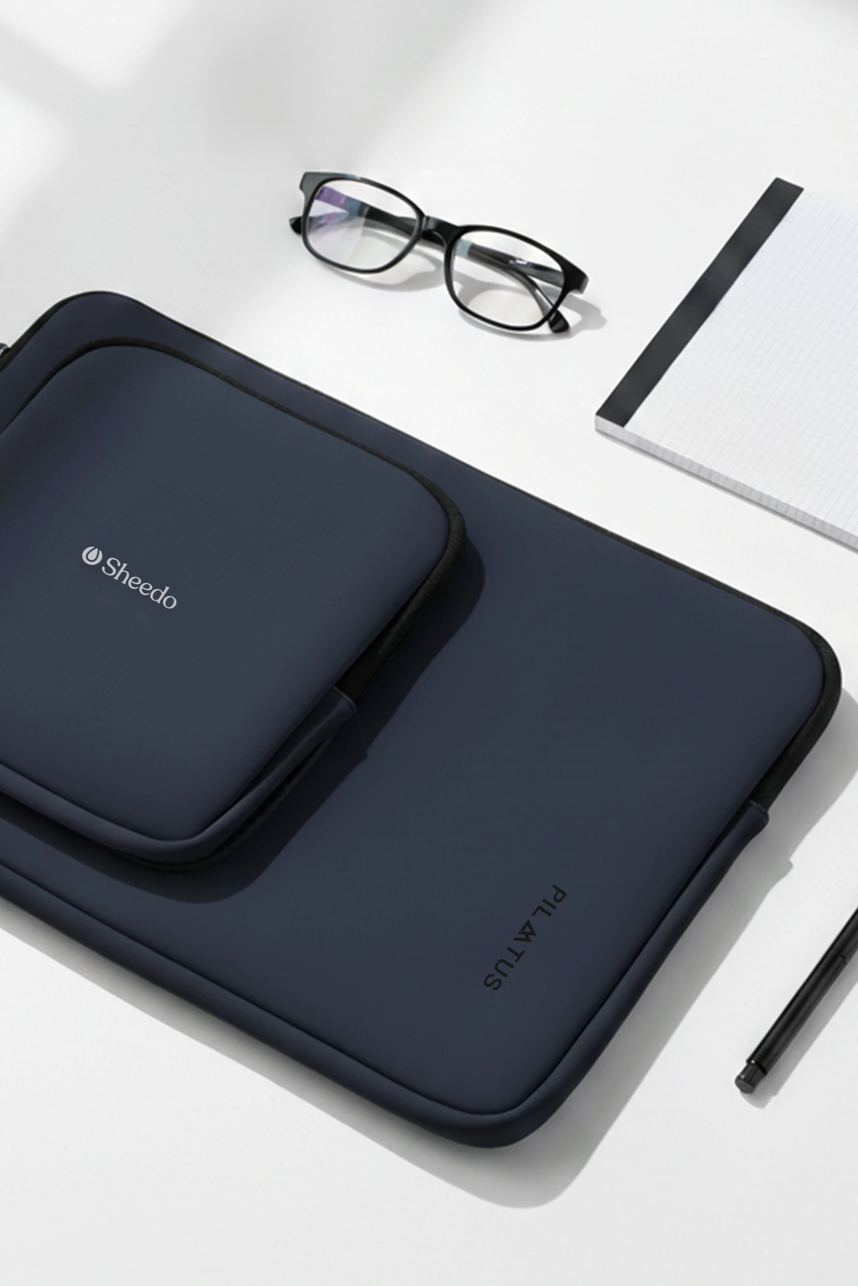 Funda de portátil - Pilatus Sleeve de 16'' pulgadas. De color azul y con personalización a una tinta. Colocada en una mesa de oficina.