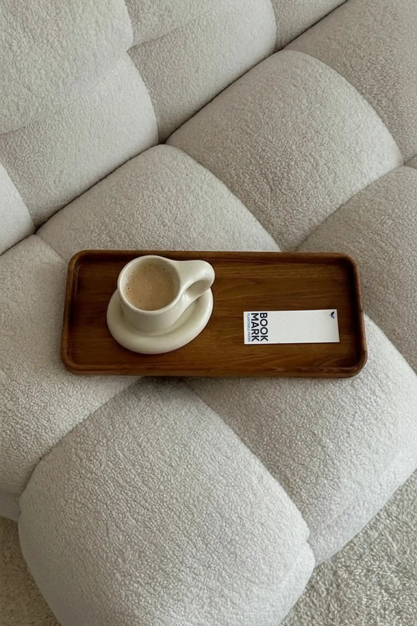 Marcapáginas de papel plantable colocado en una bandeja de madera junto con una taza de café encima de un sillón blanco.