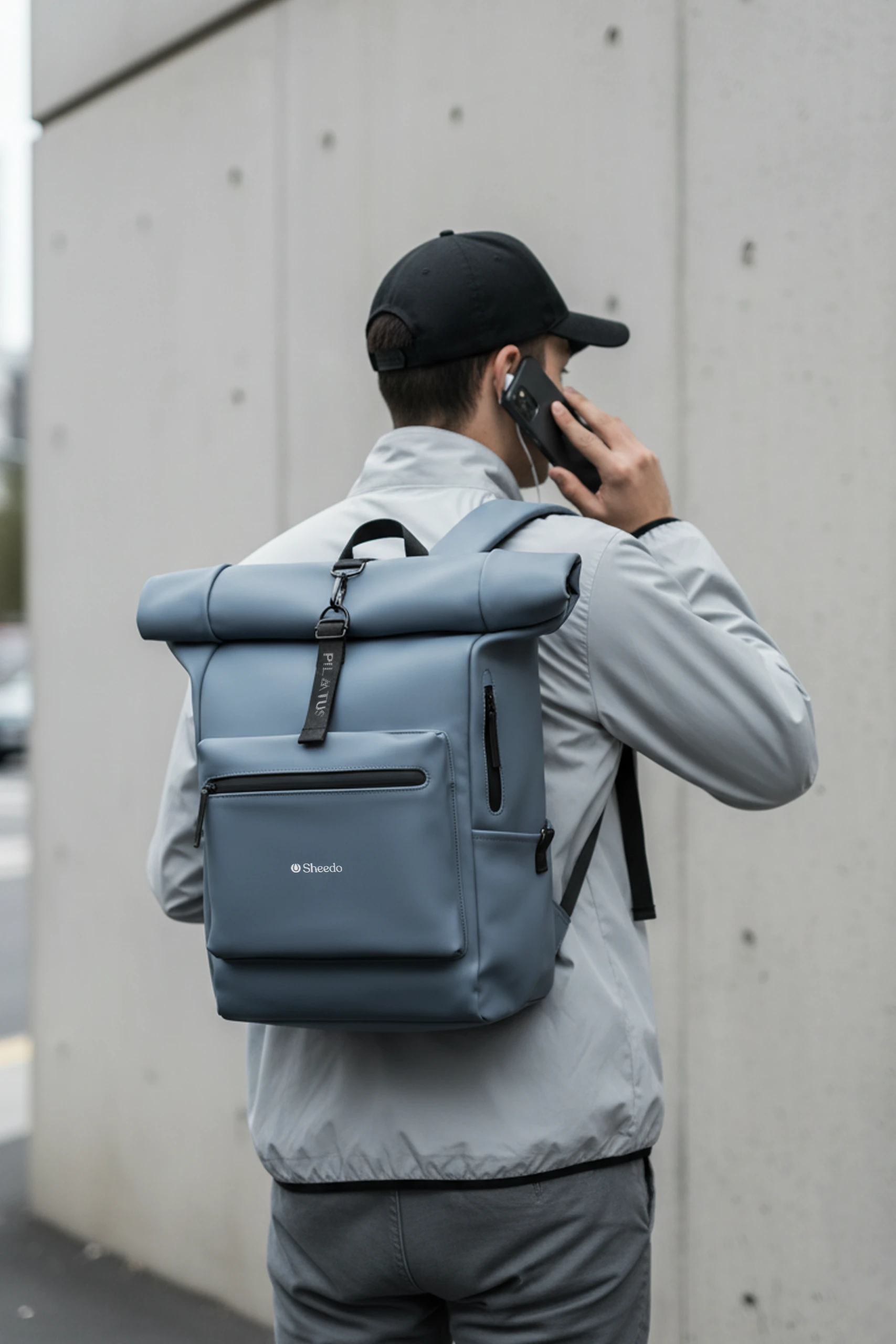 Mochila urbana y enrollable de la marca Pilatus , de color azul y con personalización a 1 tinta. Colgada de un chico que habla por teléfono.
