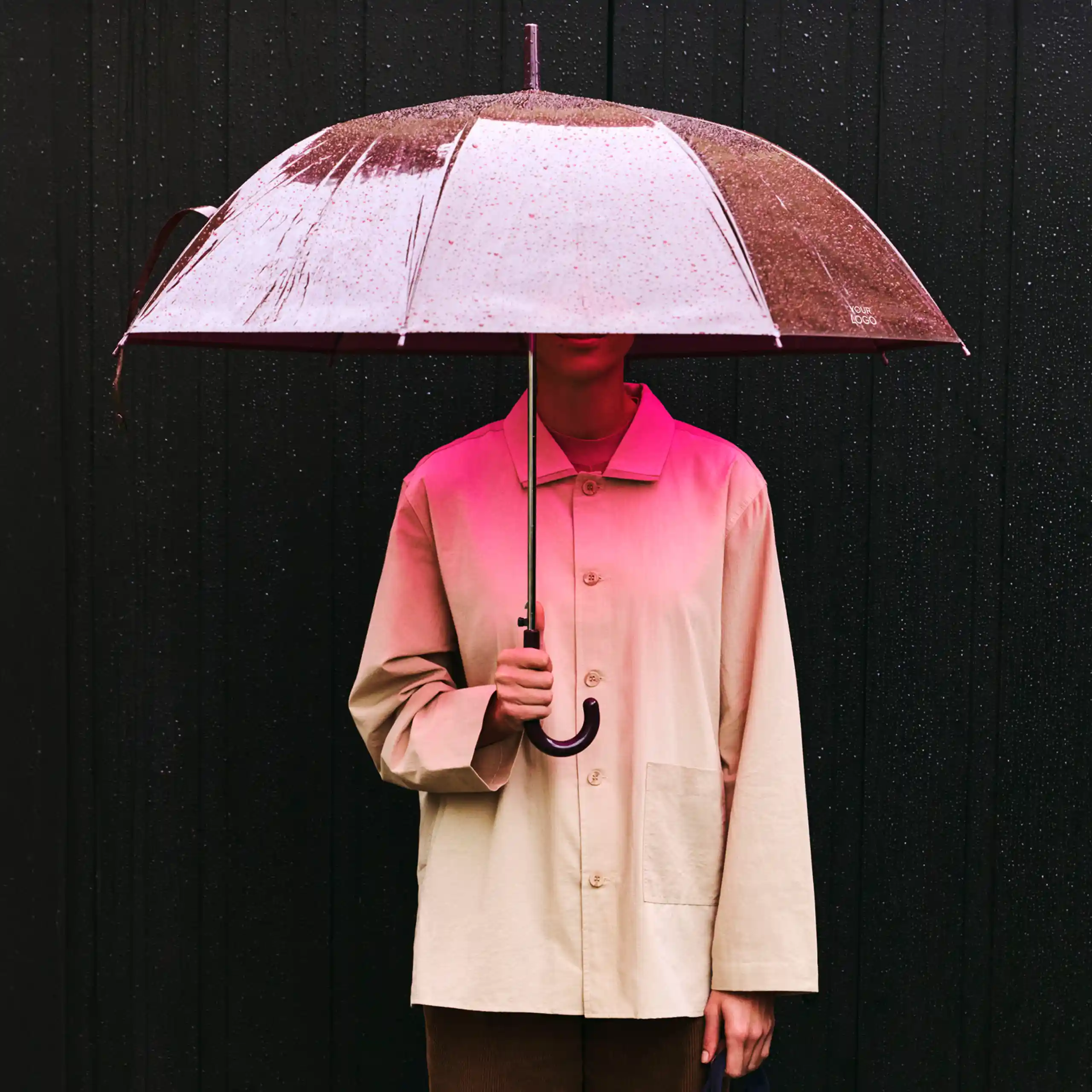 Paraguas de diseño púrpura transparente de la marca HAY. Con varillas de fibra de vidrio y mango curvado. Sujeto por una persona bajo la lluvia.