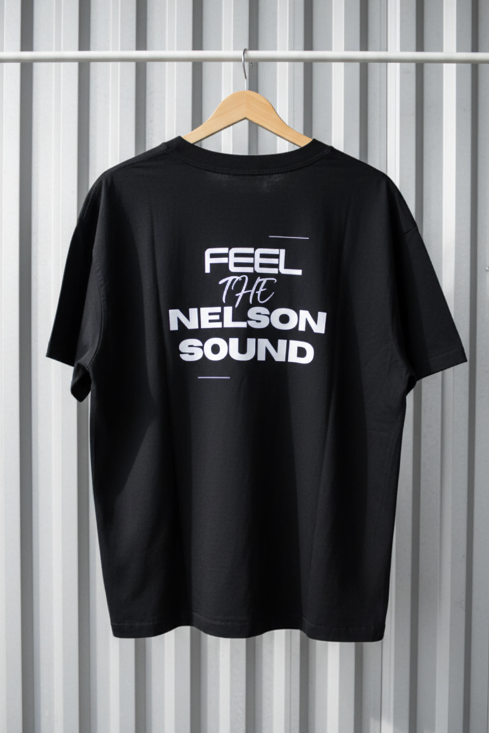 Camiseta oversize negra personalizada para la marca personal DJ Nelson, colgada de una percha de madera