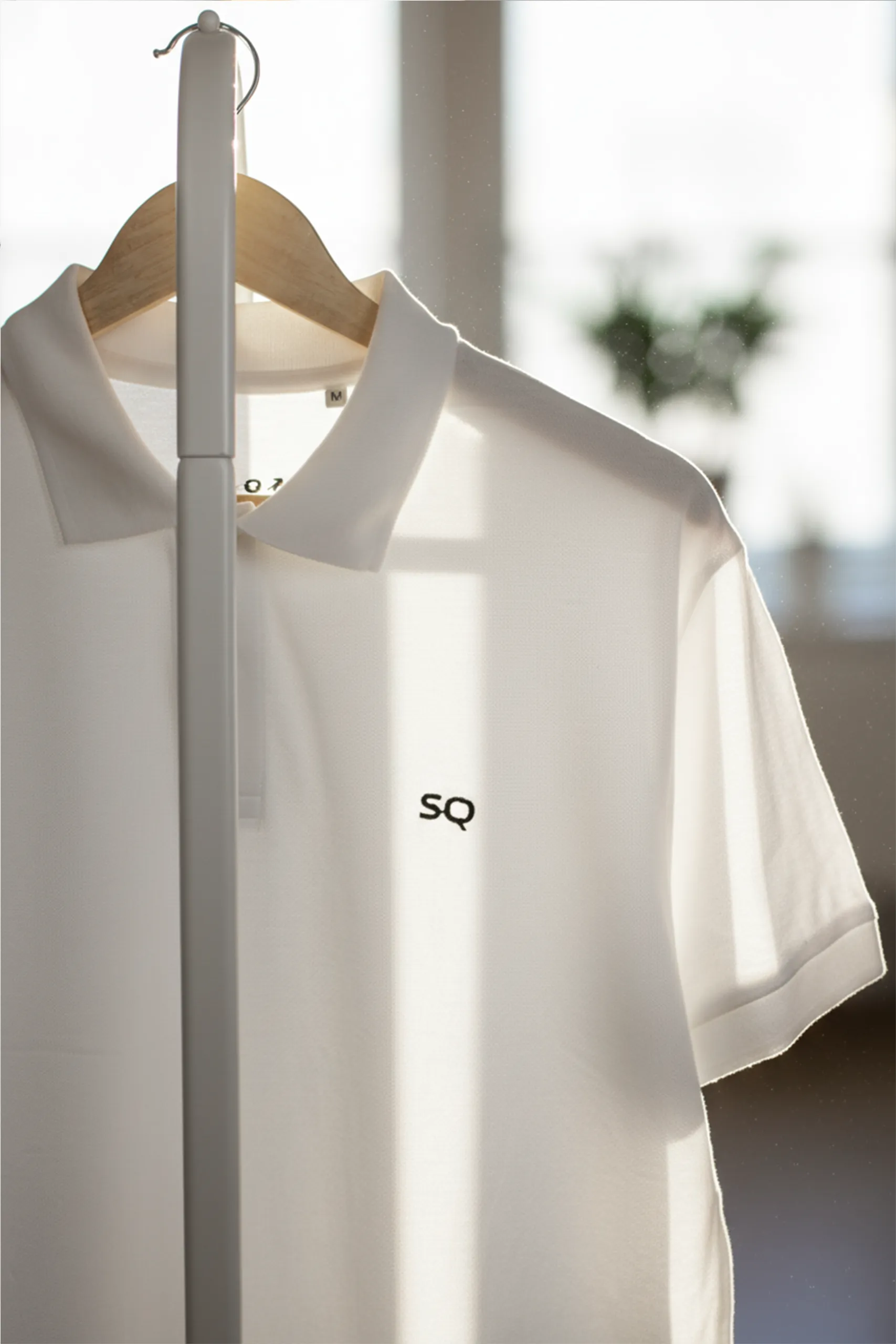 Polo blanco personalizado con el logo de la marca Sophiq Properties, colgado de una percha