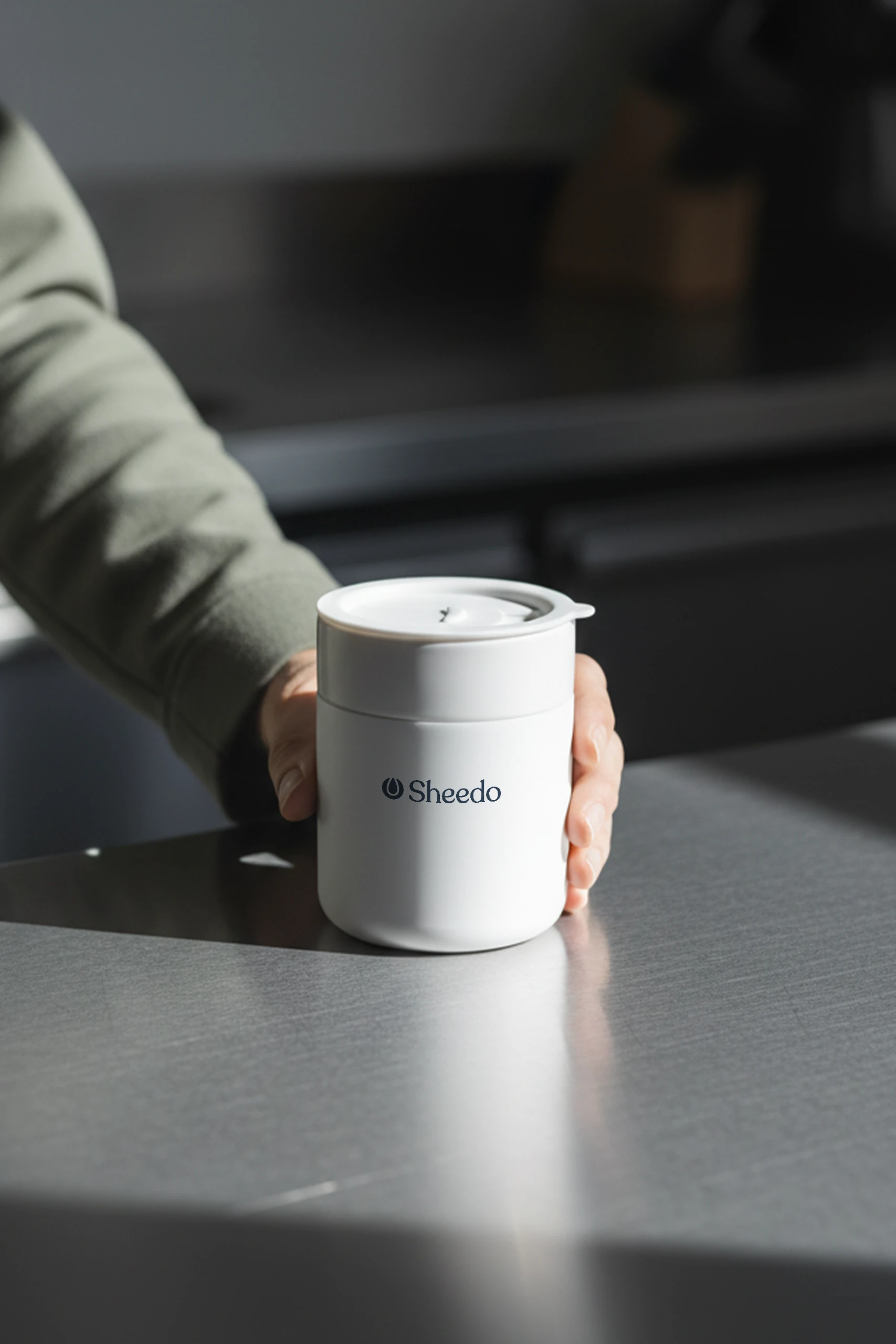 Mano sujetando un vaso de cerámica blanco personalizado con el logotipo de Sheedo